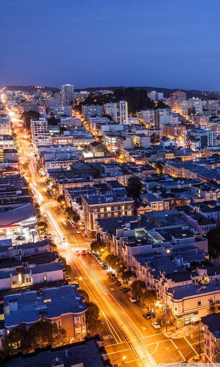 san francisco iPhone 桌布 壁紙 — 黃昏時分城市街道的鳥瞰圖，移動的汽車發出琥珀色光芒，蜿蜒穿過密集的住宅建築。