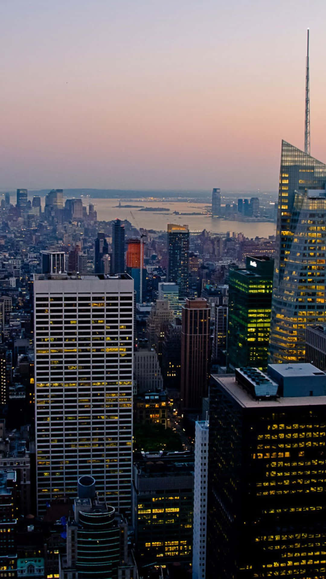 Android Ny City 桌布 壁紙 — 黃昏時分密集城市天際線的全景視圖，遠處有燈火通明的摩天大樓和閃閃發光的水濱。