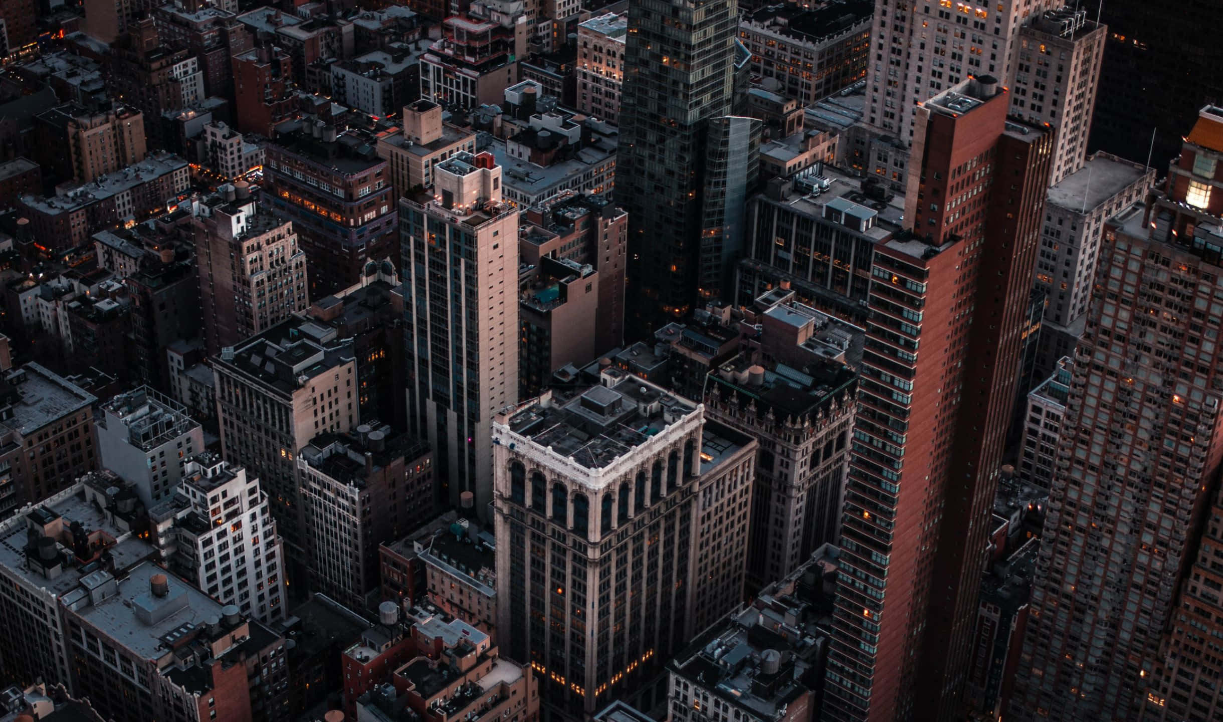 2440x1440 Empire State Building 桌布 壁紙 — 黃昏時分密集城市天際線的鳥瞰圖， illuminated 窗戶在漸暗的天空中閃耀。