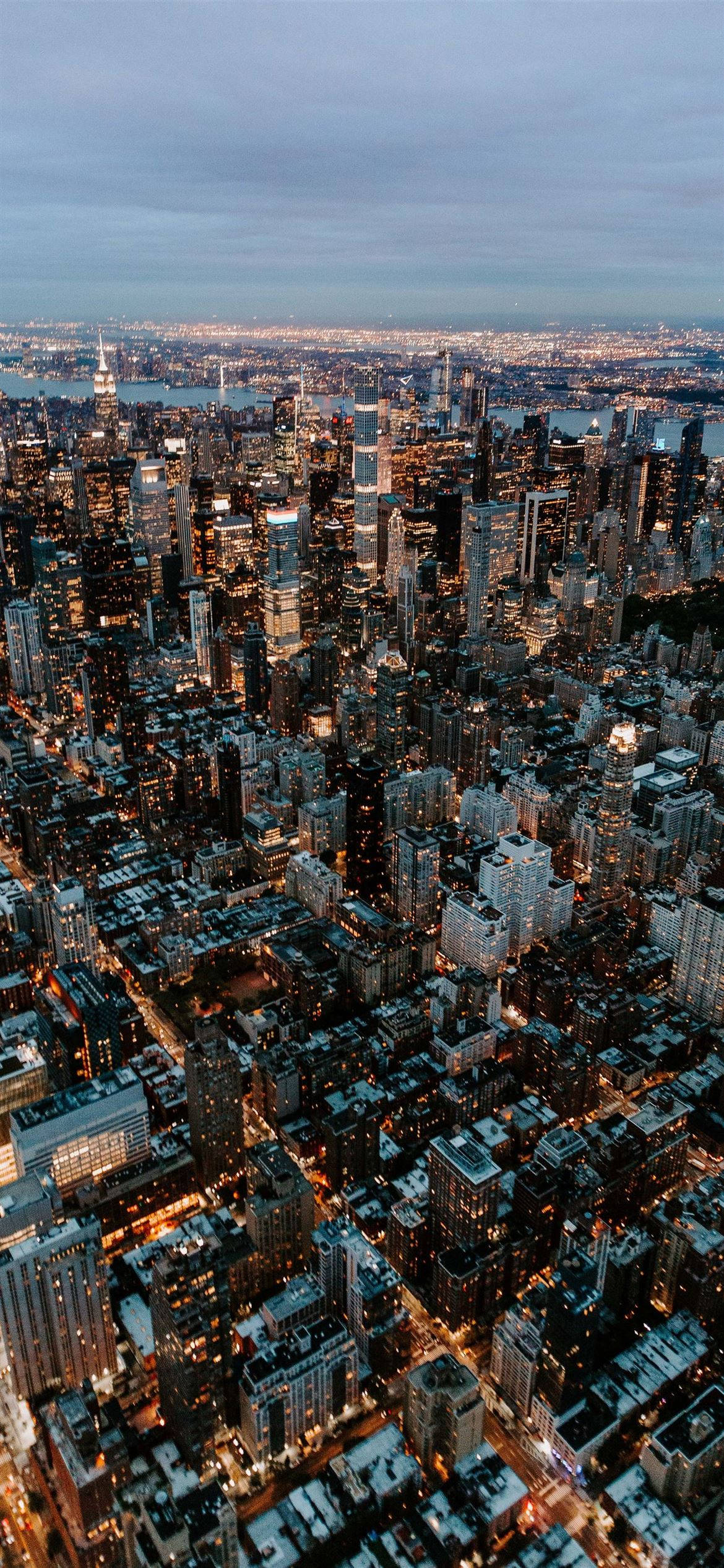 new york city iPhone x 桌布 壁紙 — 黃昏時分密集城市景觀的鳥瞰圖，帶有發光的窗戶和多雲的天空。