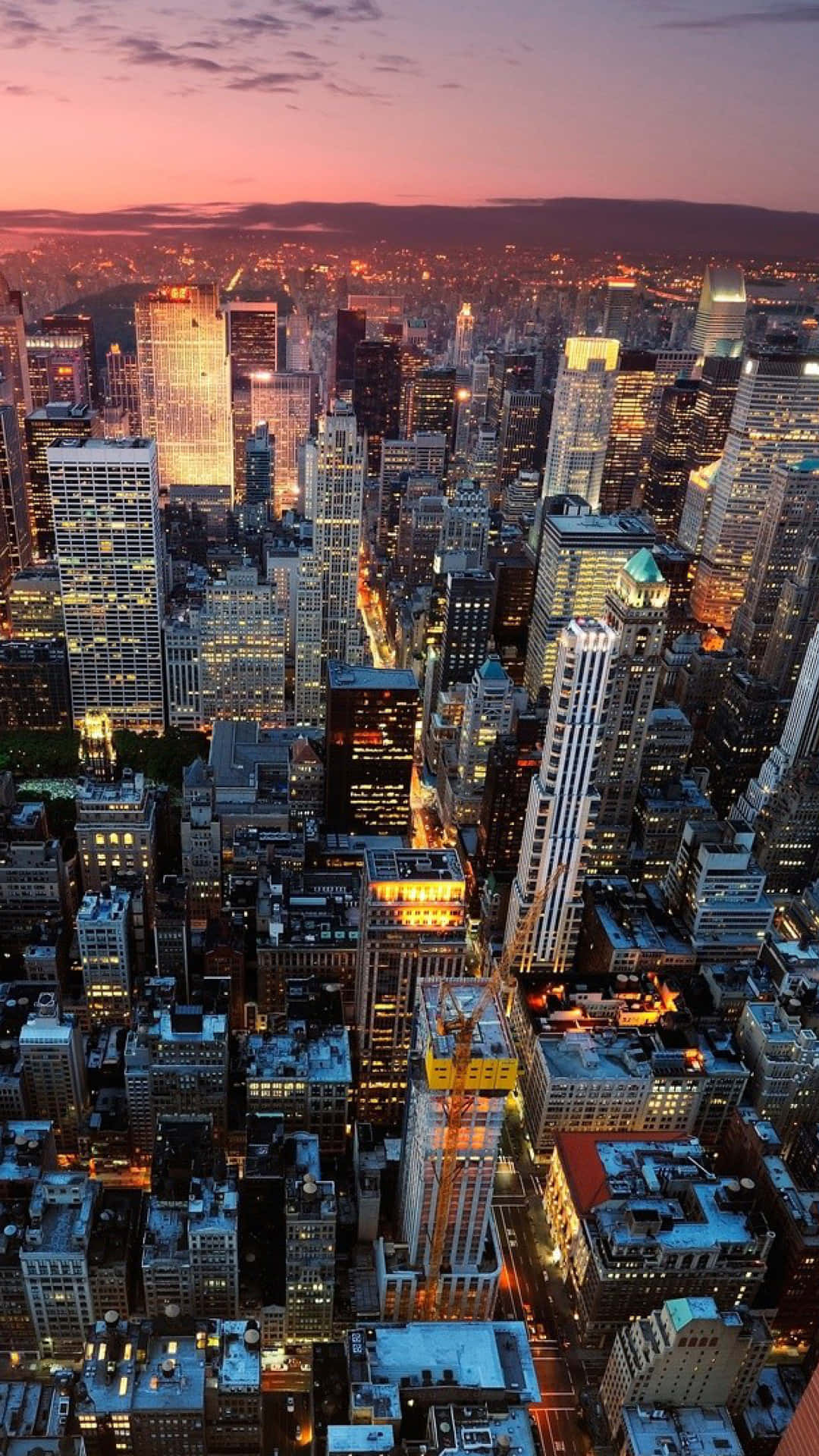 New York City Night iPhone 桌布 壁紙 — 黃昏時分密集城市景觀的鳥瞰圖，摩天大樓在粉紅色和紫色的天空中閃耀。