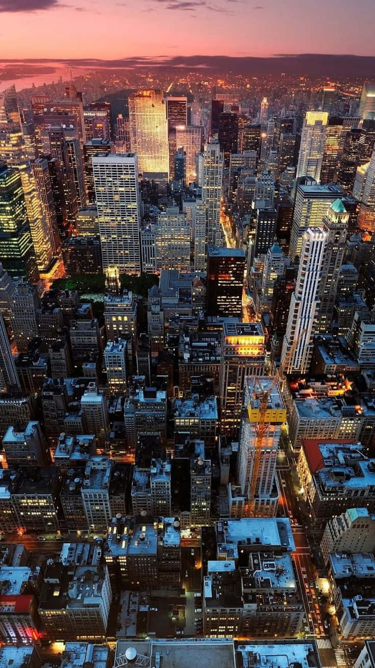 New York 桌布 壁紙 — 黃昏時分密集城市景觀的鳥瞰圖，摩天大樓在粉紅色和橙色的天空下閃耀。