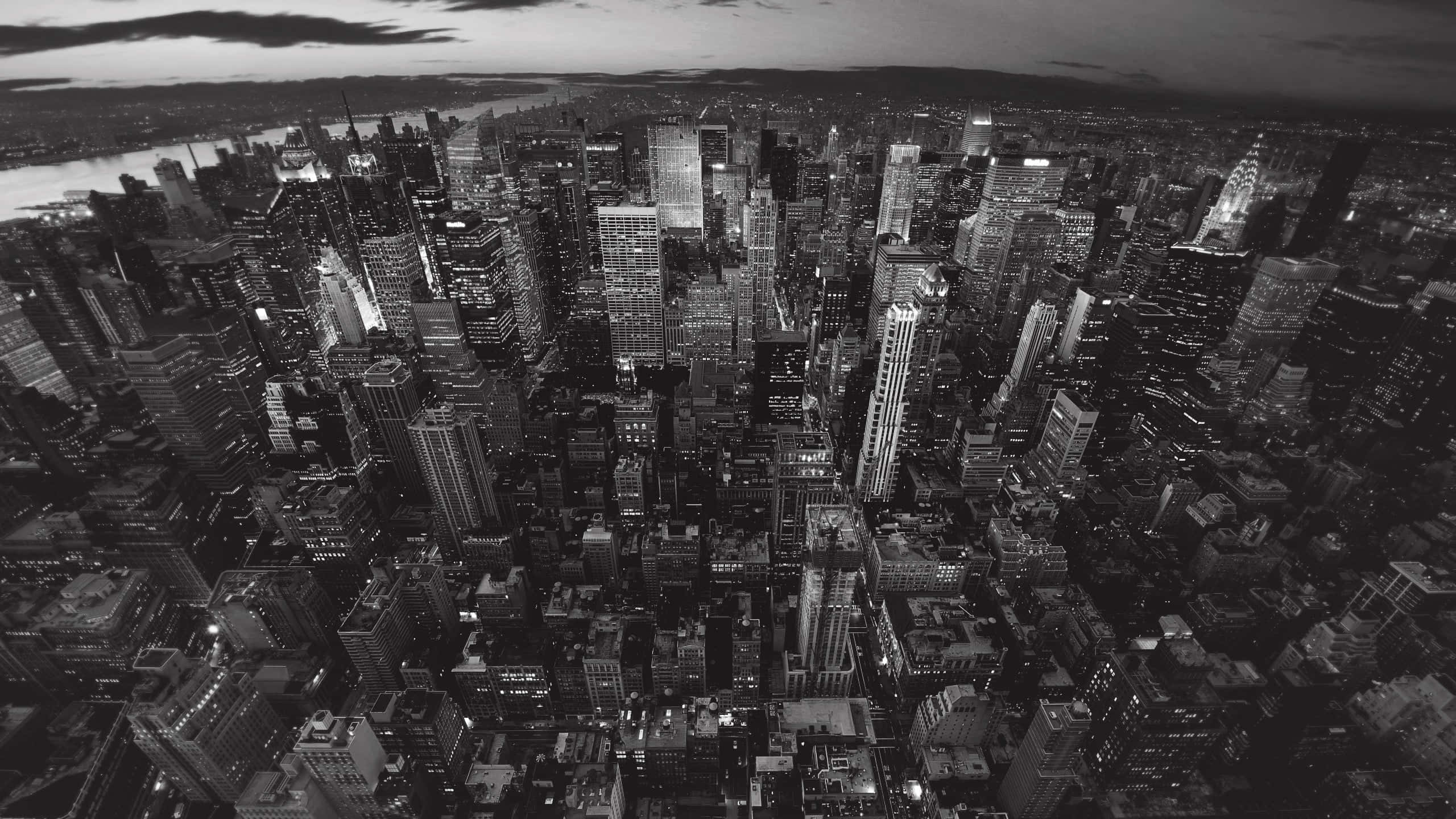 Black And White Cityscape 桌布 壁紙 — 黃昏時分密集城市景觀的黑白空拍圖，顯示了燈火通明的摩天大樓和蜿蜒穿過城市範圍的河流。