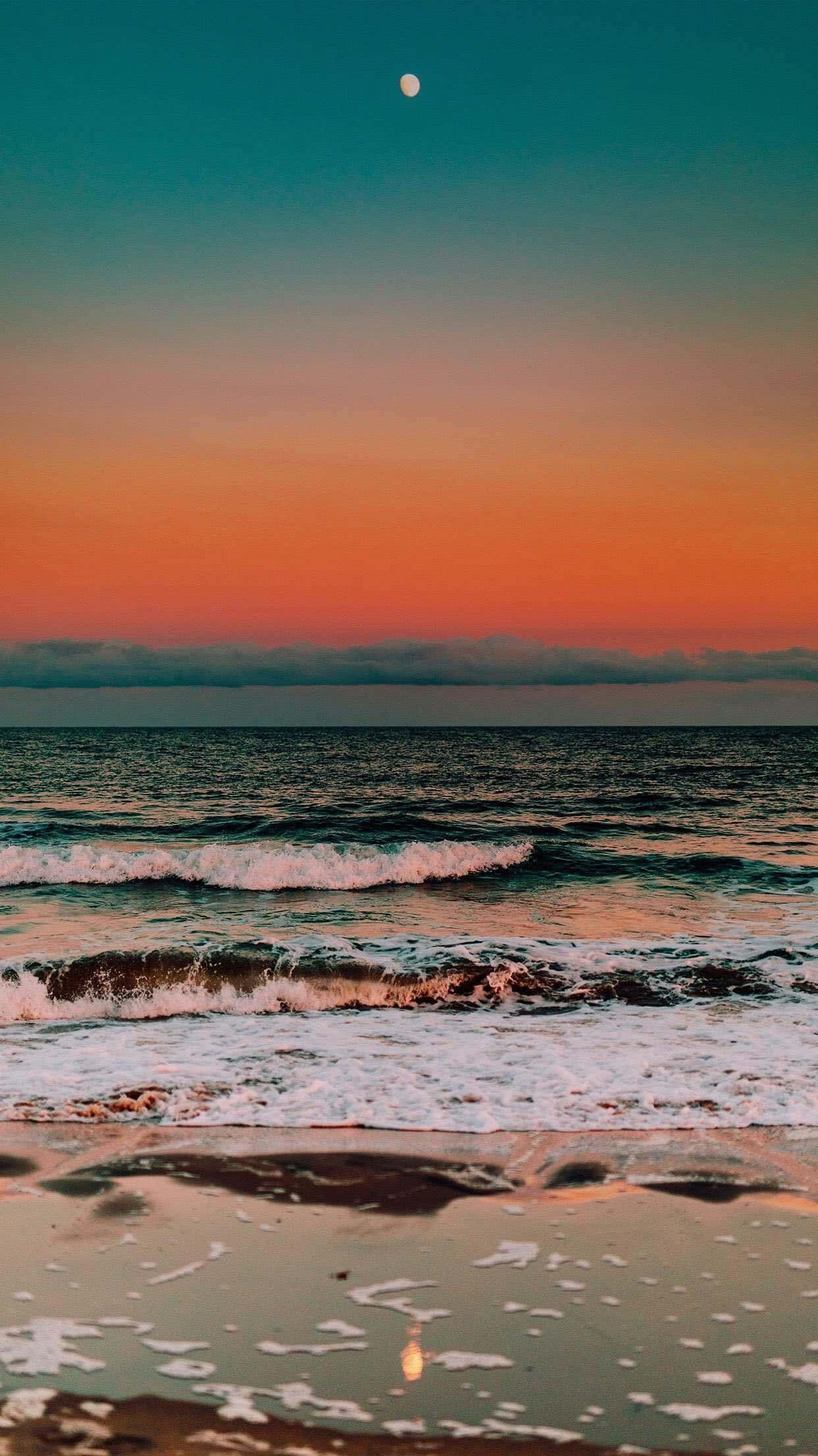 Beach Aesthetic 桌布 壁紙 — 黃昏時分寧靜的海灘，在青綠色、橙色和粉紅色的漸變天空下，溫柔的海浪翻滾而來，月亮清晰可見。