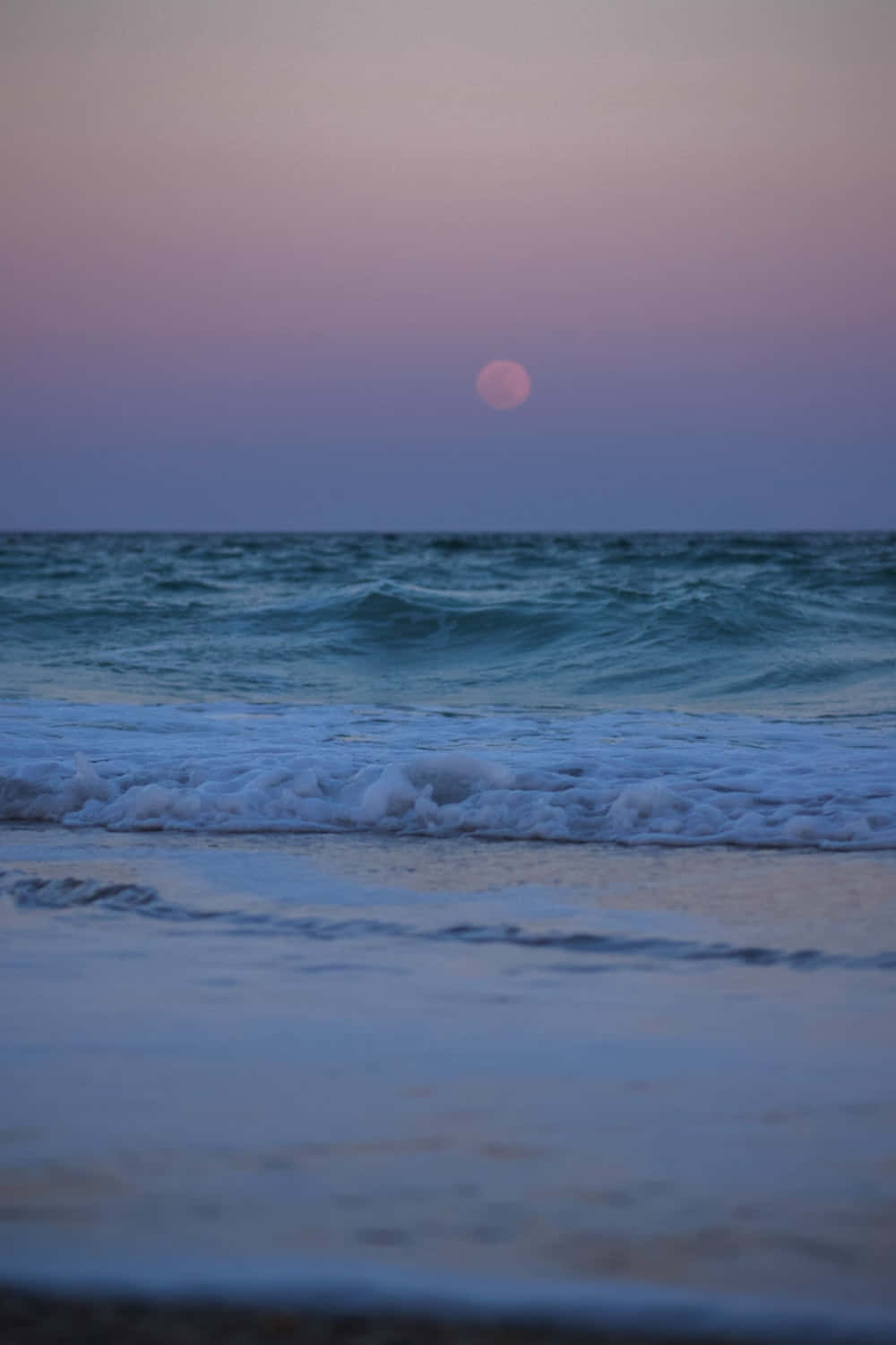 Beach Aesthetic 桌布 壁紙 — 黃昏時分寧靜的海灘，溫柔的海浪在柔和的粉紅色和紫色天空下拍打著海岸，一輪明月閃耀。
