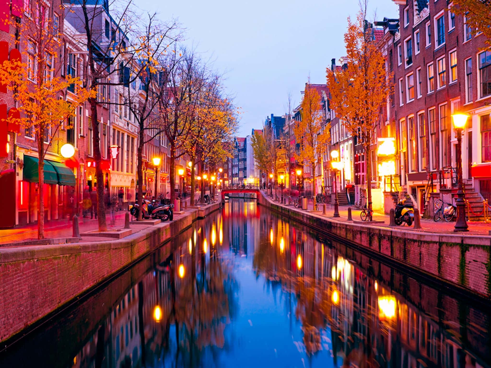 Red Light District 桌布 壁紙 — 黃昏時分寧靜的阿姆斯特丹運河，溫暖的街燈倒映在平靜的水面上，兩旁是歷史悠久的磚砌建築和秋樹。