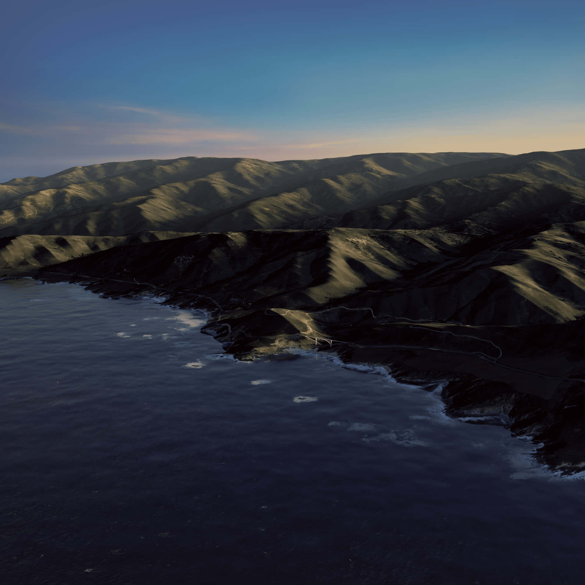 macOS Big Sur 動態桌布 桌布 壁紙 — 黃昏時分崎嶇海岸山脈的鳥瞰圖，蜿蜒的道路緊貼懸崖，襯托著深藍色的海洋。