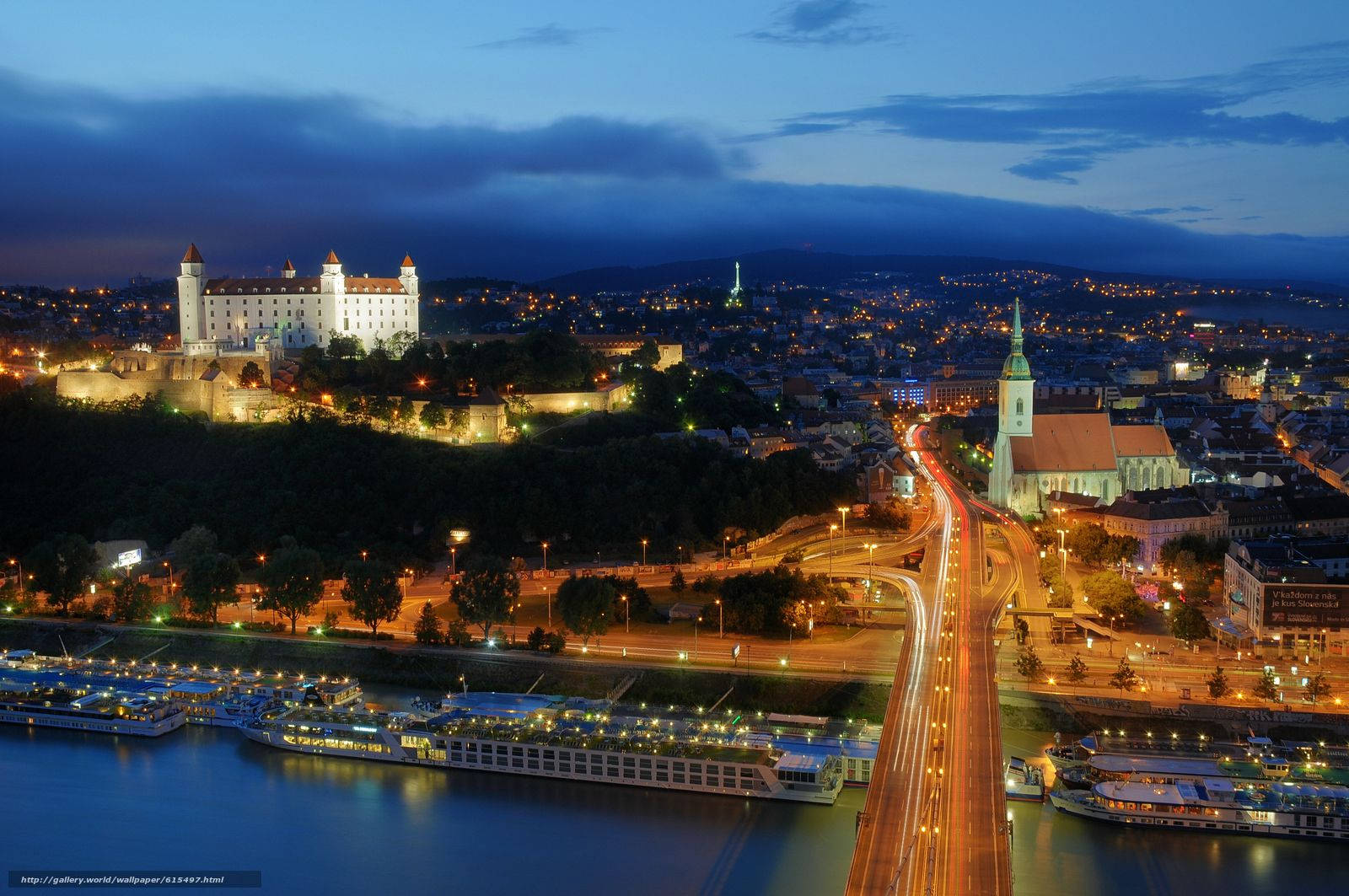 Slovakia 桌布 壁紙 — 黃昏時分布拉迪斯拉發的鳥瞰圖，城堡亮起燈光，俯瞰河上的船隻和發光的城市街道。