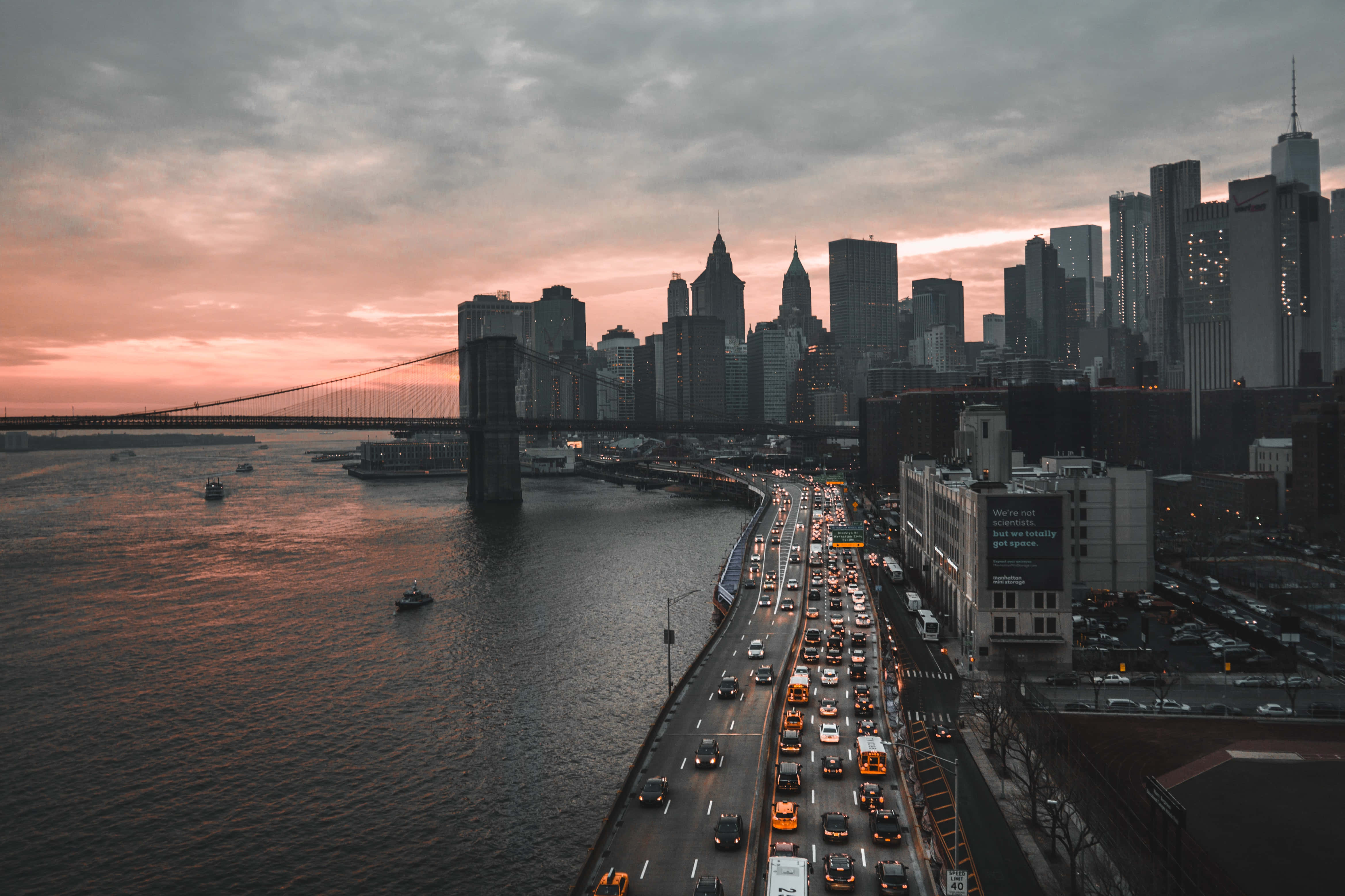 Nyc 桌布 壁紙 — 黃昏時分布魯克林大橋的航拍圖，交通在粉紅色和灰色的天空下流動，背景是紐約市的天際線。