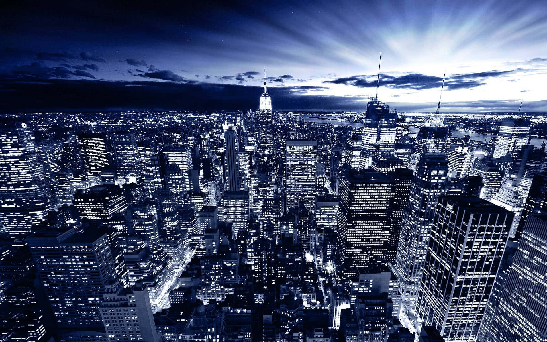 Nyc 桌布 壁紙 — 黃昏時分廣闊城市景觀的單色藍色航拍圖，閃爍的摩天大樓和戲劇性的天空光線。