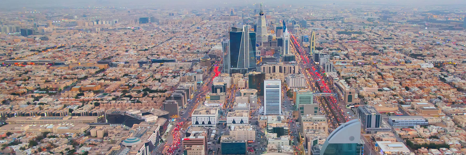 Riyadh 桌布 壁紙 — 黃昏時分廣闊城市景觀的鳥瞰圖，發光的車流和摩天大樓刺穿朦朧的天空。