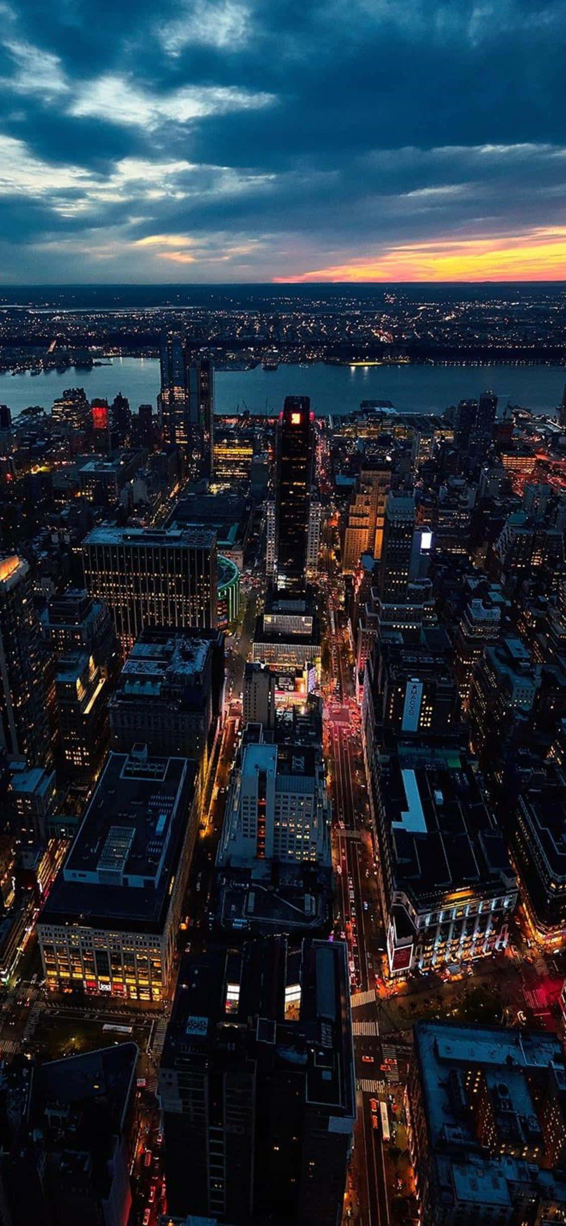iPhone X 桌布 壁紙 — 黃昏時分廣闊城市景觀的鳥瞰圖，閃爍的摩天大樓和水面上充滿活力的橙色地平線。