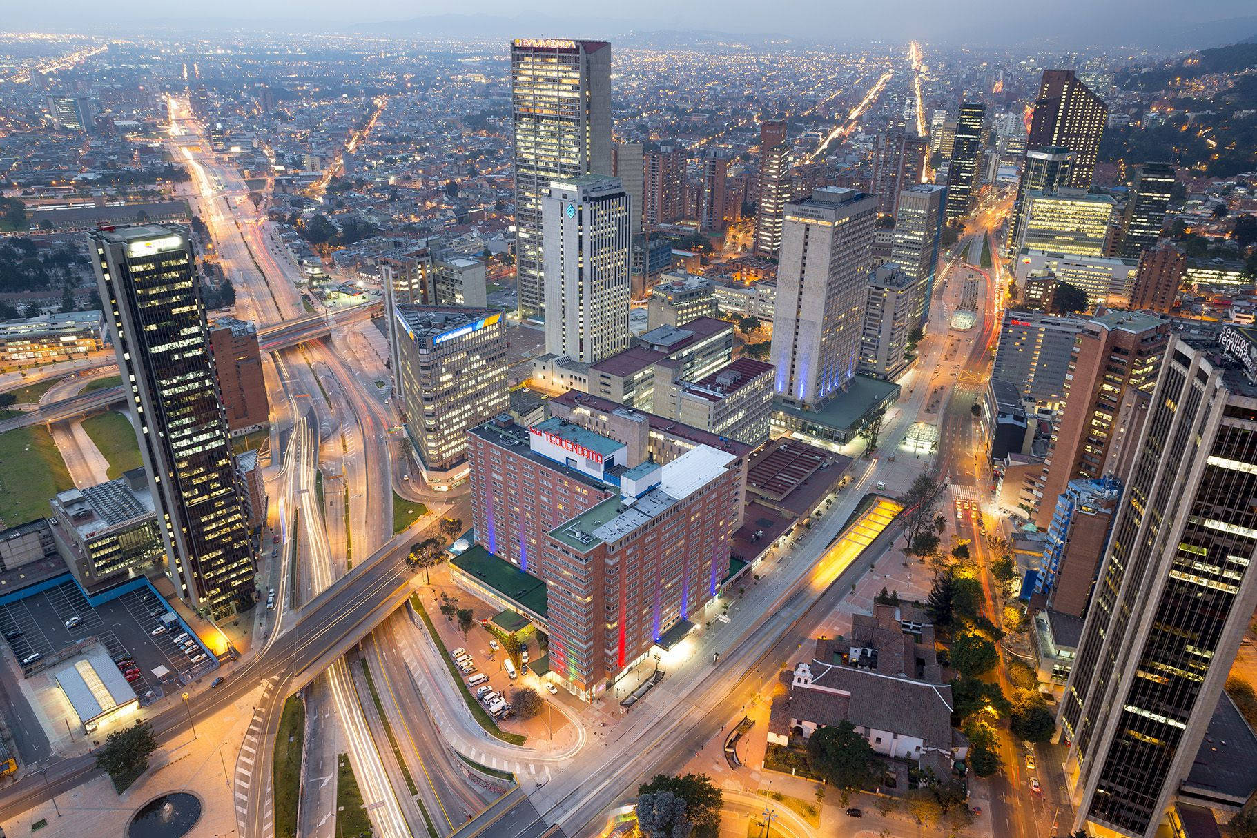 Bogota 桌布 壁紙 — 黃昏時分廣闊城市景觀的鳥瞰圖，閃爍的摩天大樓和照明的高速公路蜿蜒穿過密集的城市建築。