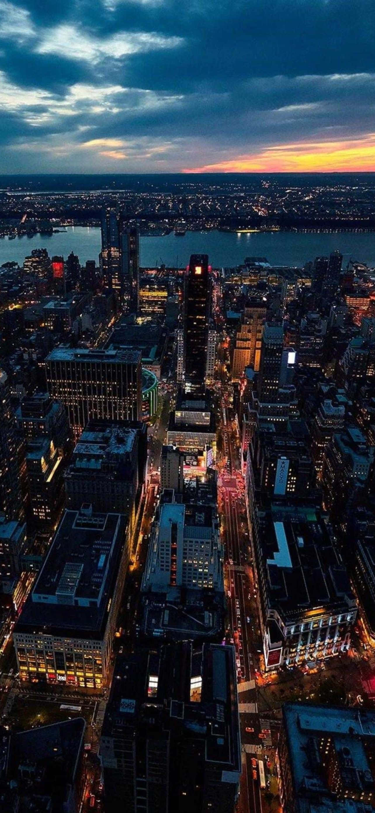 酷炫iPhone 桌布 壁紙 — 黃昏時分廣闊城市景觀的鳥瞰圖，閃爍的摩天大樓和河流映照著逐漸褪色的橙色日落。