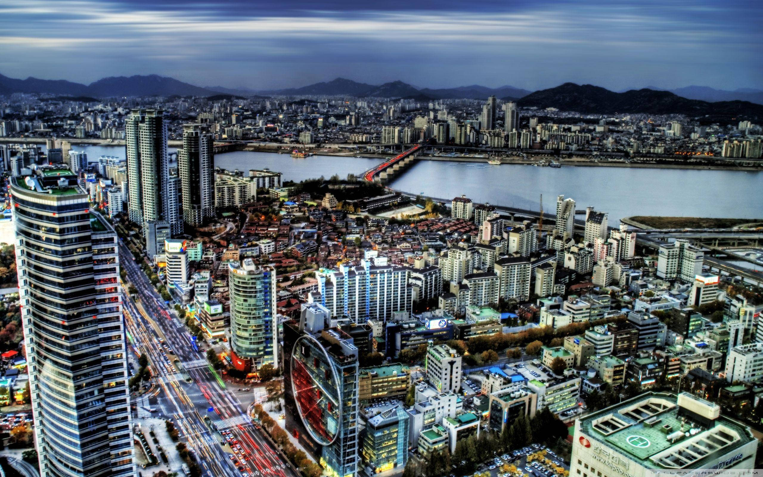 South Korea 桌布 壁紙 — 黃昏時分廣闊城市景觀的鳥瞰圖，閃爍的摩天大樓和河橋在陰沉天空下。