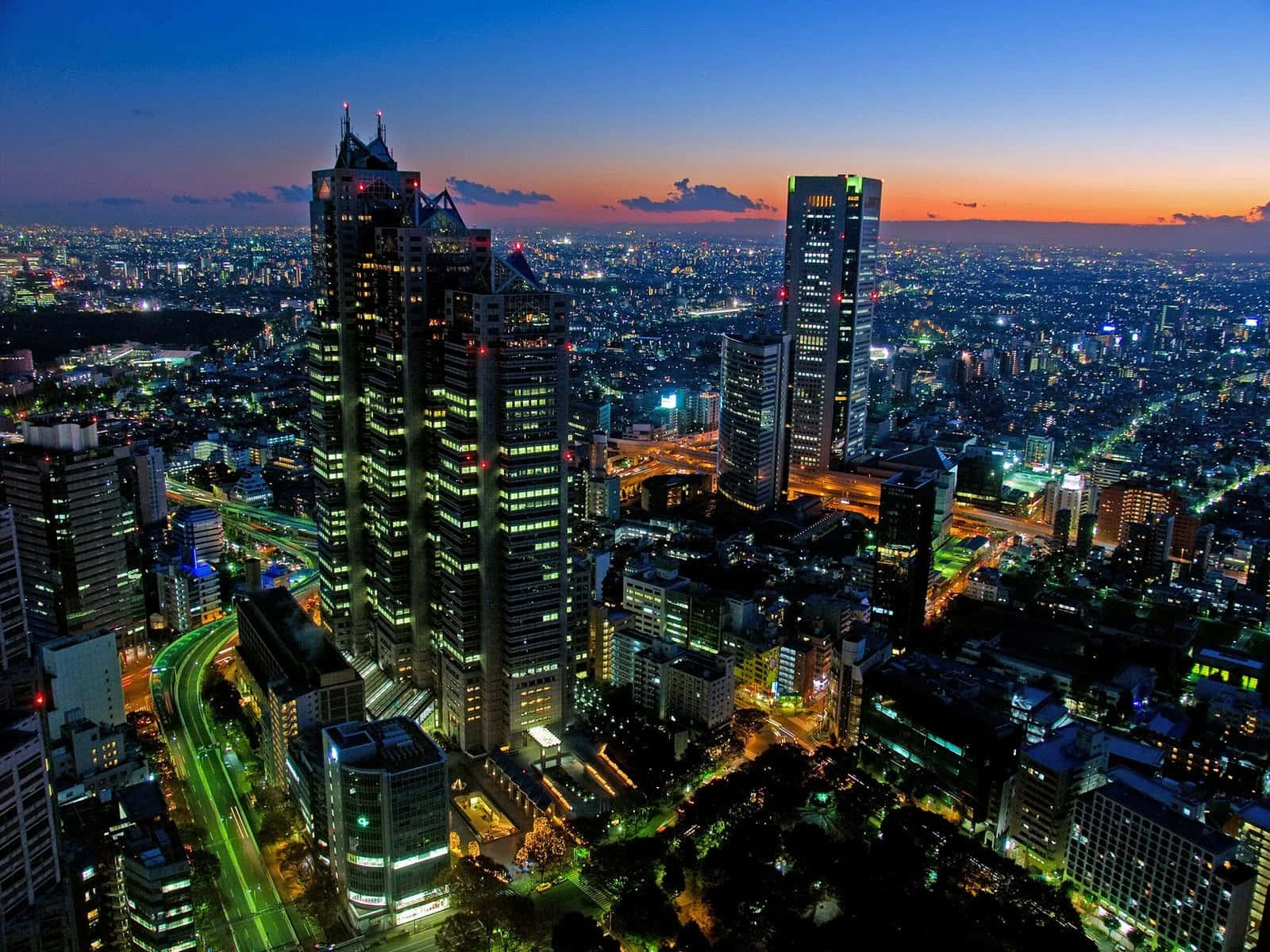 Buildings 桌布 壁紙 — 黃昏時分廣闊城市景觀的鳥瞰圖，高聳的摩天大樓在漸變色的天空下閃耀。