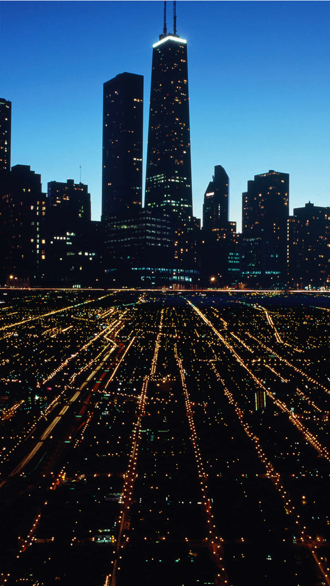 Chicago City Night 桌布 壁紙 — 黃昏時分廣闊城市的鳥瞰圖，下方有燈火通明的摩天大樓和發光的街道網格。
