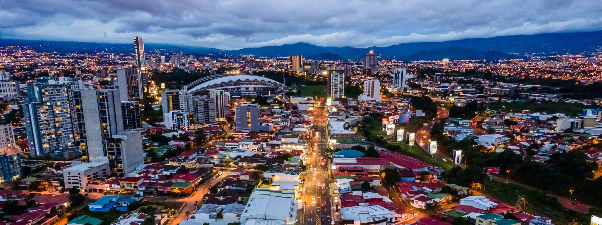 夜景城市 桌布 壁紙 — 黃昏時分廣闊城市的鳥瞰圖，多雲的天空下閃爍的街燈和建築物。