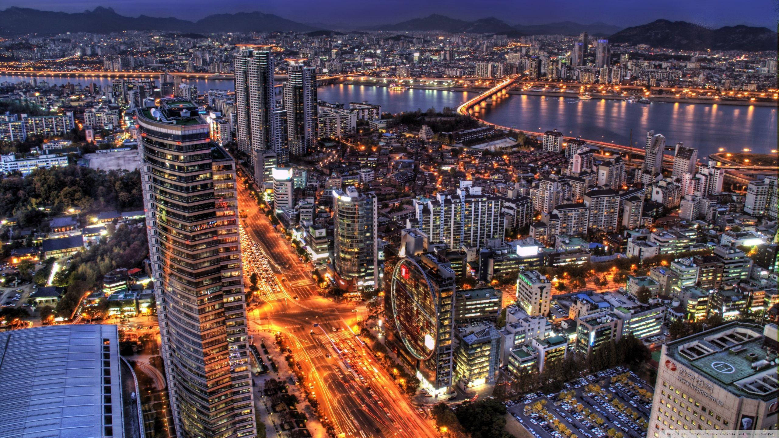 South Korea 桌布 壁紙 — 黃昏時分廣闊城市的鳥瞰圖，摩天大樓閃爍，河畔橋樑被溫暖的燈光照亮。