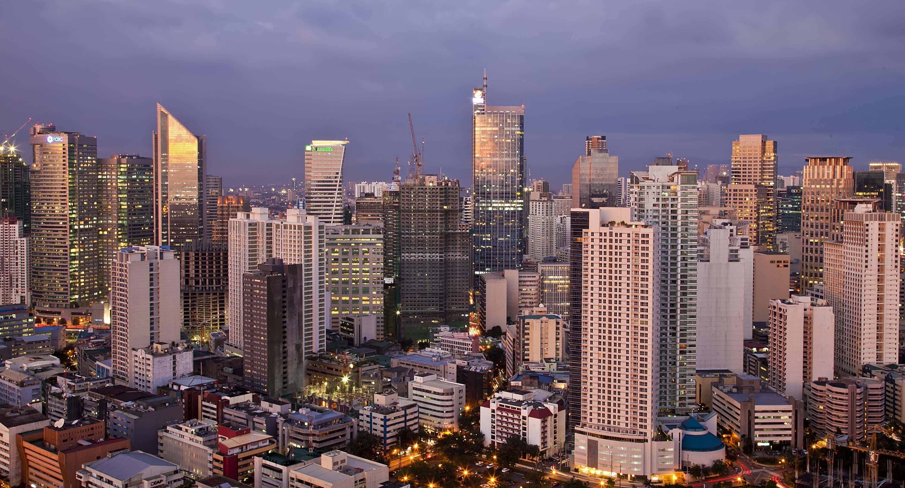 Manila 桌布 壁紙 — 黃昏時分廣闊的城市天際線，高聳的摩天大樓在深紫色天空的映襯下閃耀。