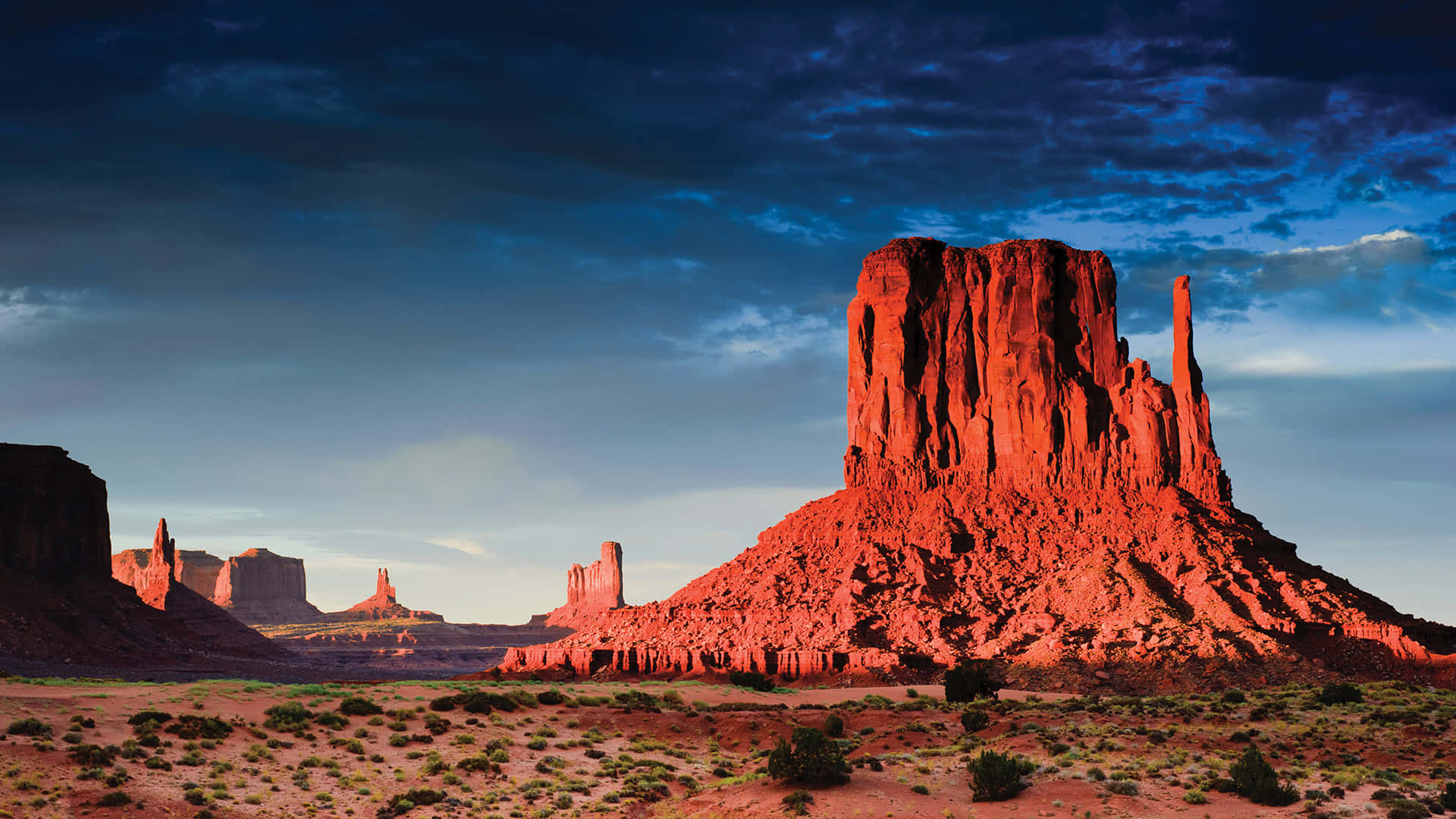 Arizona 桌布 壁紙 — 黃昏時分戲劇性的沙漠景觀，高聳的紅色岩層在憂鬱的藍天映襯下呈現剪影。