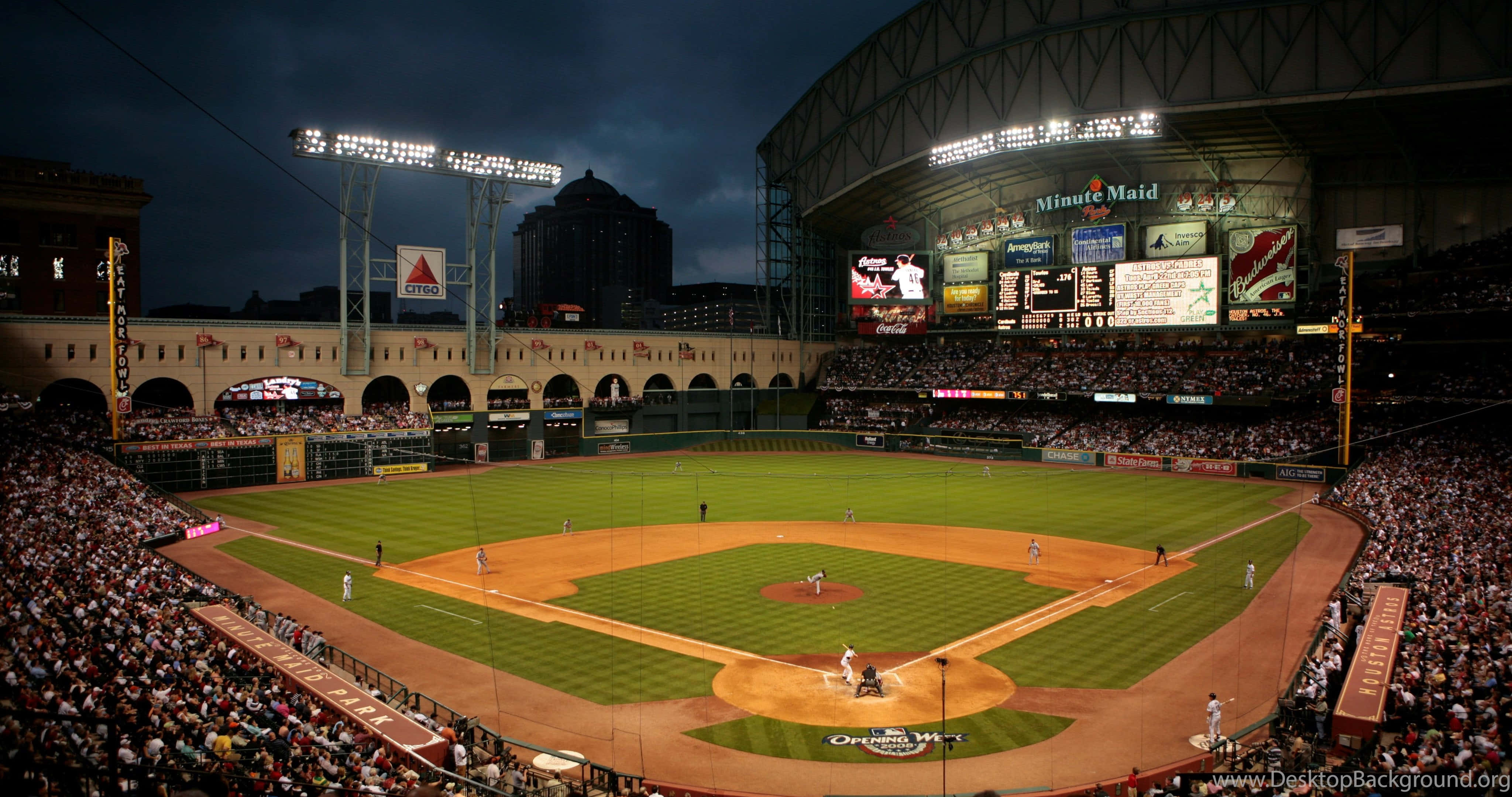Baseball Field 桌布 壁紙 — 黃昏時分擠滿人的棒球場，場上有球員，明亮的燈光照亮綠色草地和泥土內野。