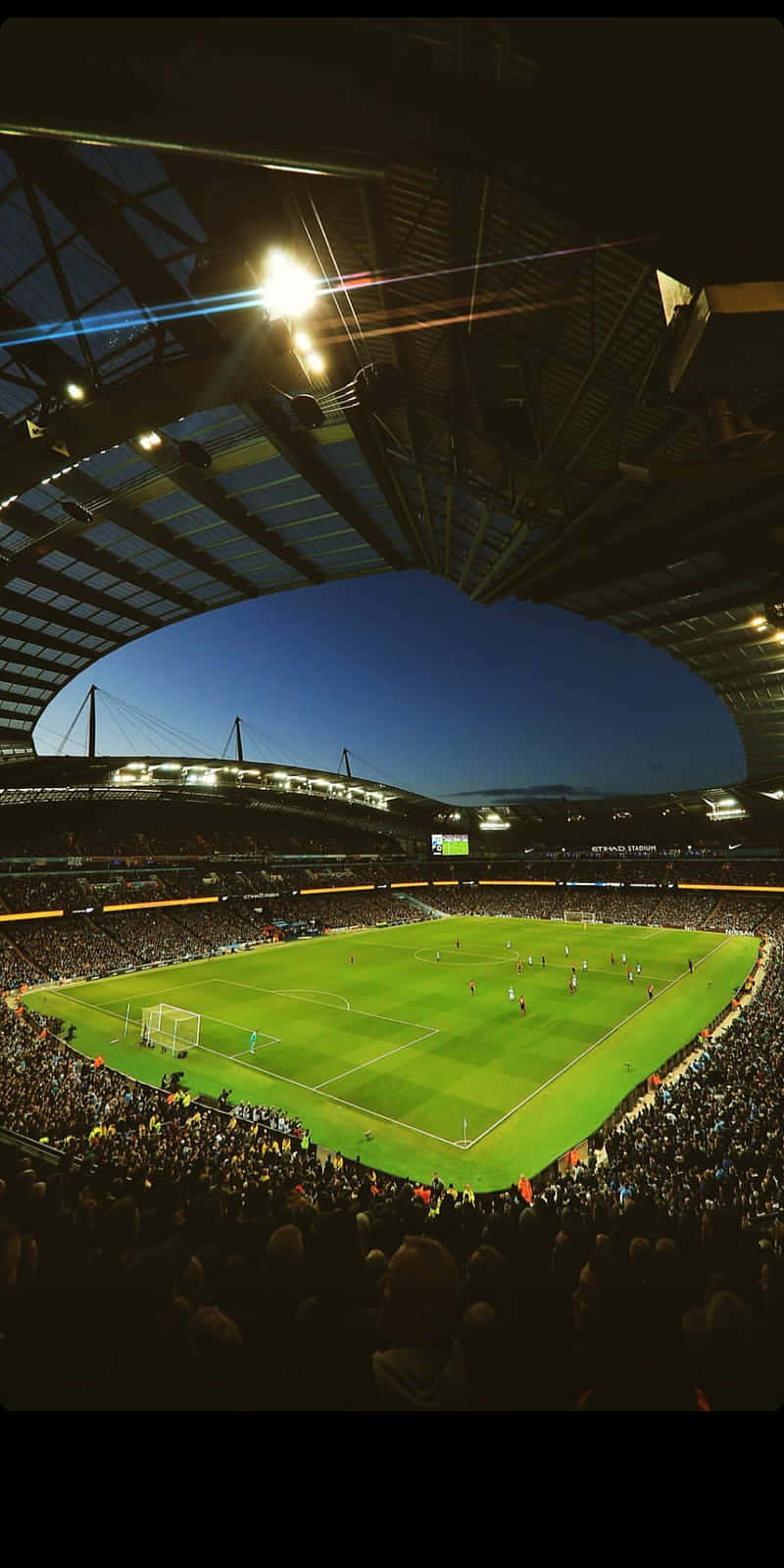 Soccer Stadium 桌布 壁紙 — 黃昏時分擠滿觀眾的足球場鳥瞰圖，明亮的泛光燈照亮了充滿活力的綠色球場。