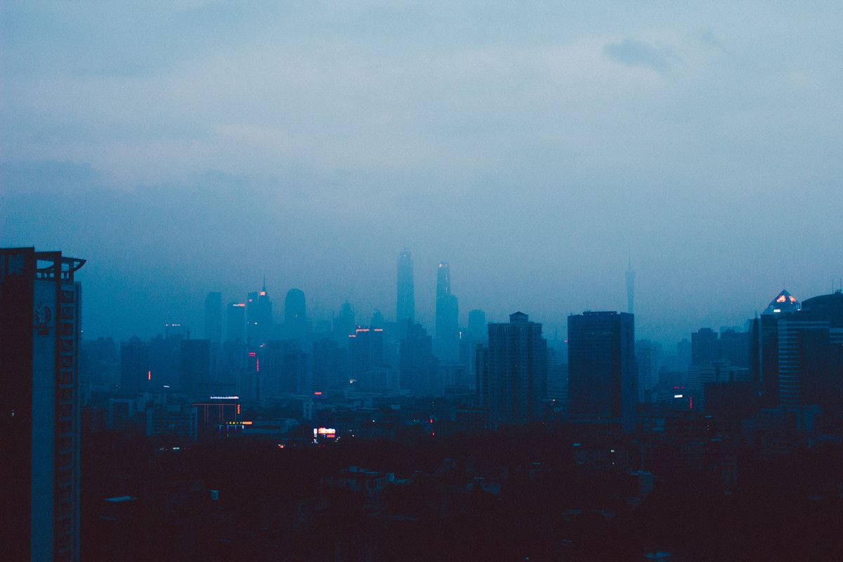 lofi 桌布 壁紙 — 黃昏時分朦朧的城市天際線，帶有柔和的藍色調和建築物散發的零星紅光。