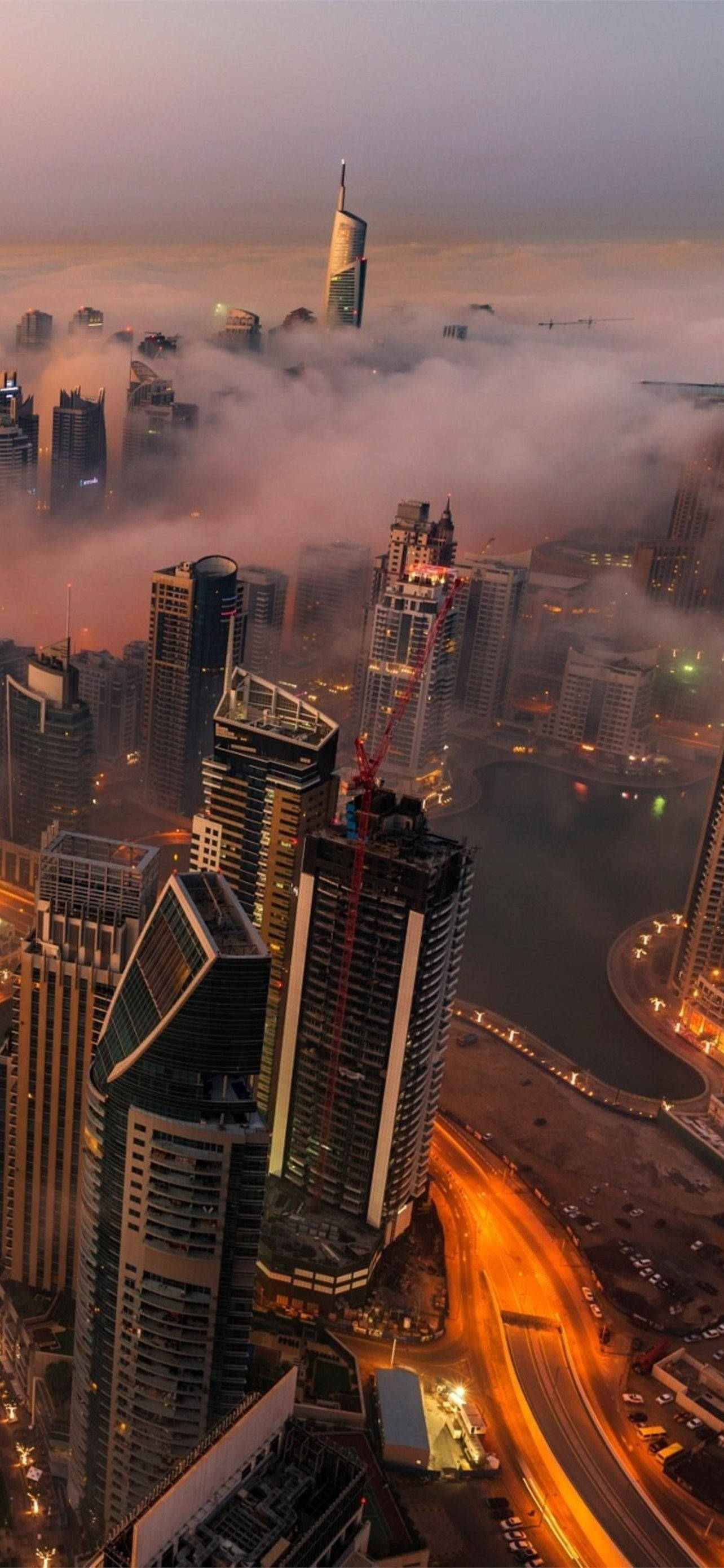 Kuwait 桌布 壁紙 — 黃昏時分未來城市景觀的鳥瞰圖，摩天大樓穿過發光的雲層，下方是燈火通明的道路。