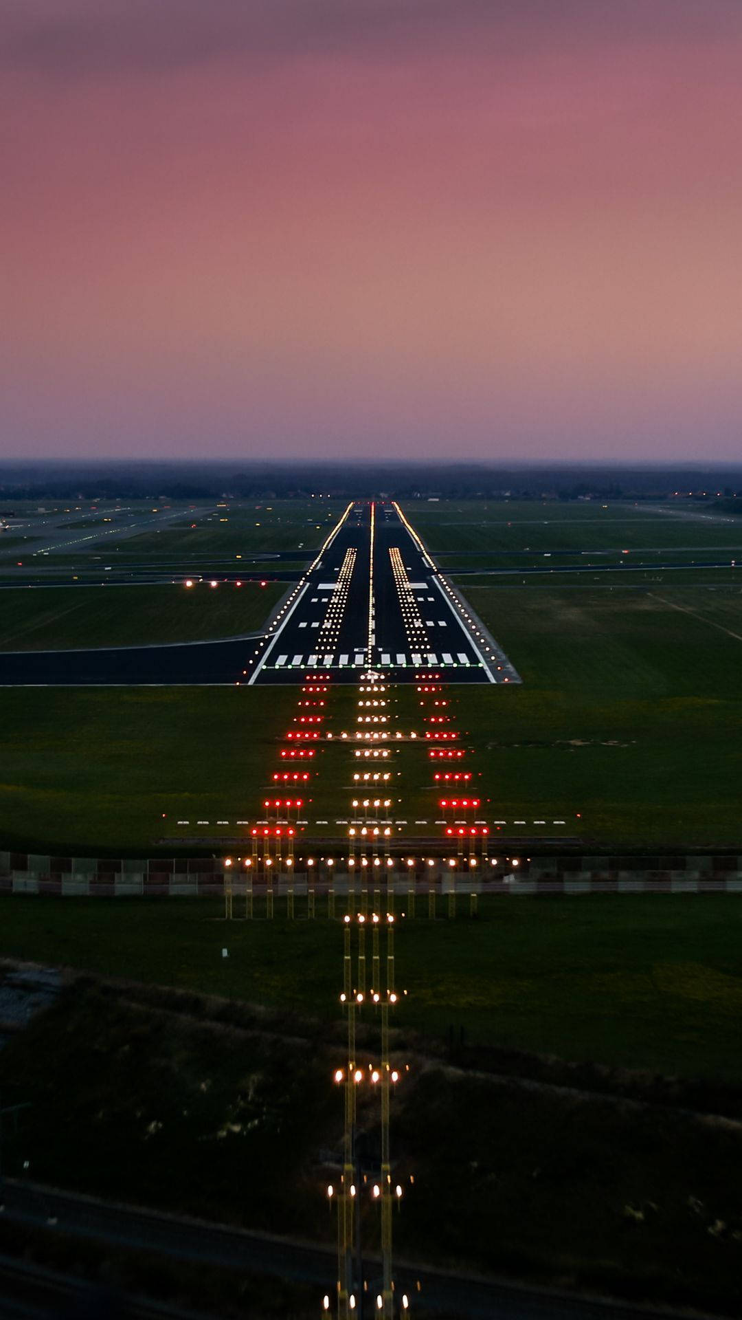 Runway 桌布 壁紙 — 黃昏時分機場跑道的鳥瞰圖，發光的燈光延伸至紫色的天空。