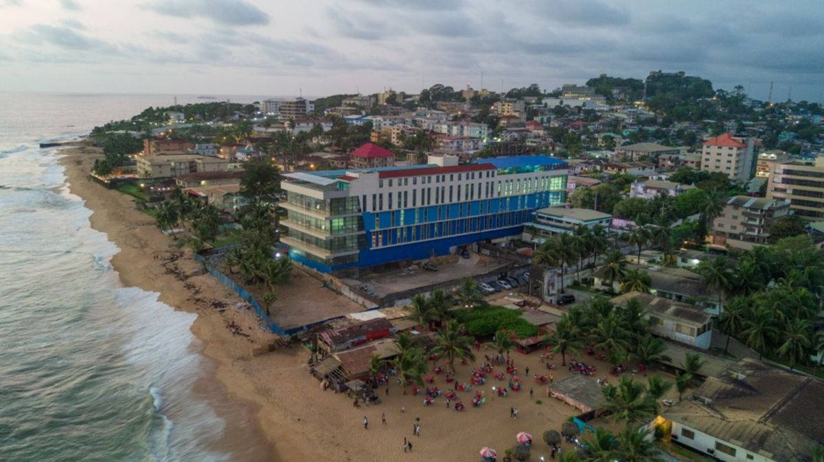 Liberia 桌布 壁紙 — 黃昏時分沿海小鎮的鳥瞰圖，沙灘和棕櫚樹旁有一座大型藍色飯店。