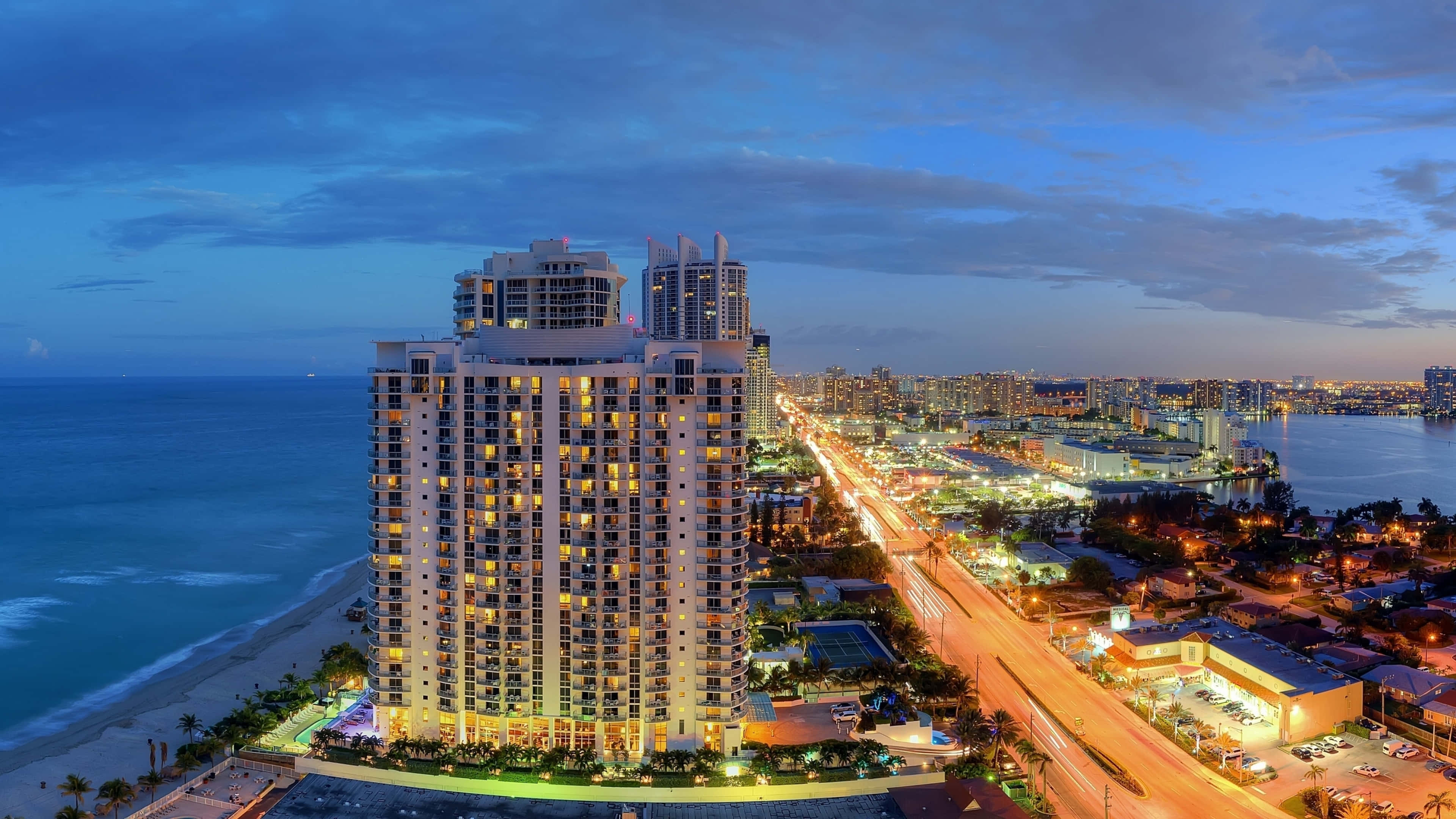 Miami 4K 桌布 壁紙 — 黃昏時分海灘旁發光的高層飯店的鳥瞰圖，城市燈光與海浪。