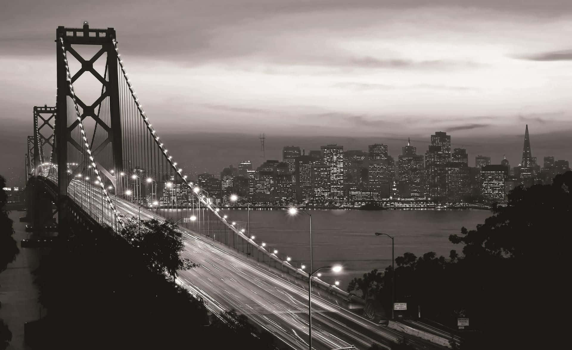 San Francisco Black And White 桌布 壁紙 — 黃昏時分海灣大橋的黑白景觀，車燈形成條紋，背景是燈火通明的城市天際線。
