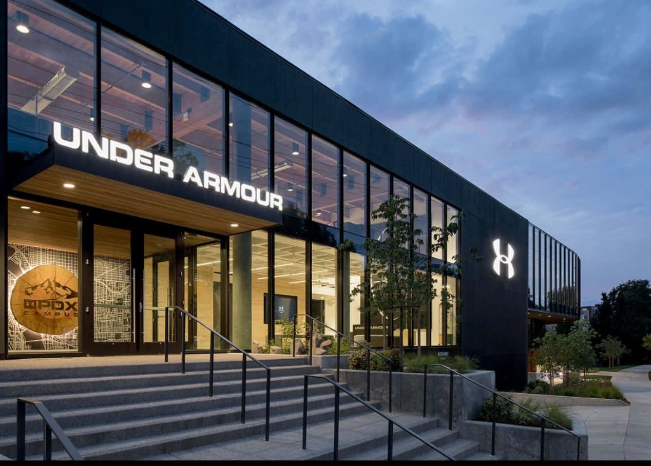 Under Armour 桌布 壁紙 — 黃昏時分現代Under Armour店舖外觀，發光招牌和玻璃窗透出室內燈光。