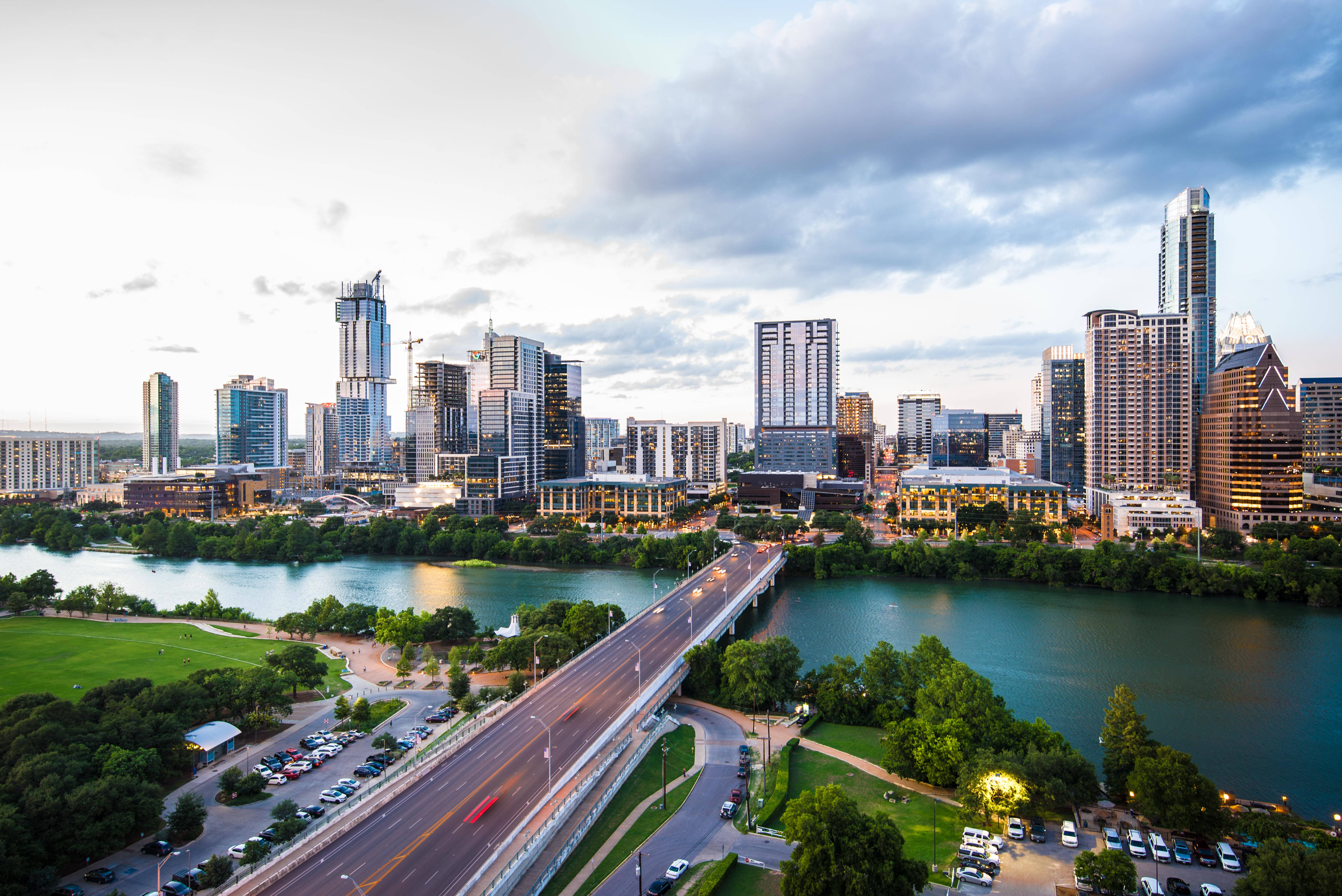Texas 桌布 壁紙 — 黃昏時分現代城市天際線的鳥瞰圖，河流流經綠色公園，橋樑承載交通。