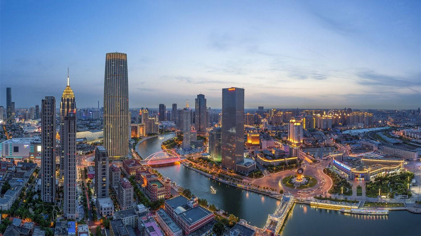 Tianjin 桌布 壁紙 — 黃昏時分現代城市景觀的鳥瞰圖，燈火通明的摩天大樓和一條發光的河流蜿蜒穿過城市建築。