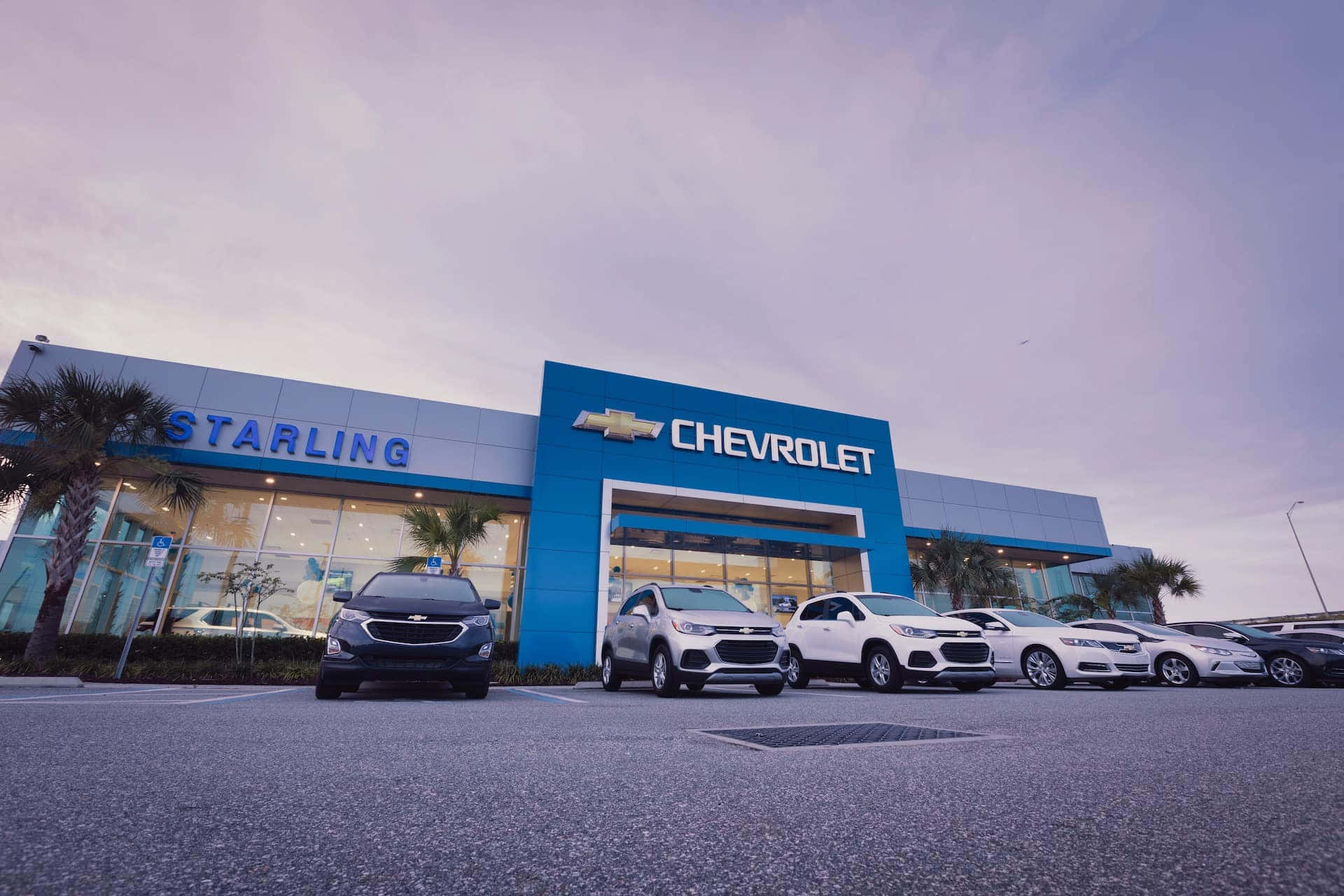 Chevrolet 桌布 壁紙 — 黃昏時分現代雪佛蘭經銷商的低角度視圖，前方停著一排SUV和轎車。