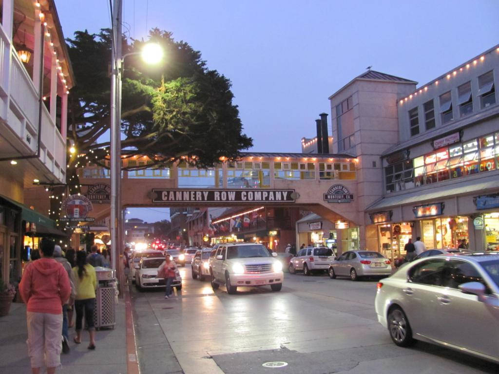 Evening 桌布 壁紙 — 黃昏時分的Cannery Row，大樹和拱門下閃爍的街燈、汽車和行人。