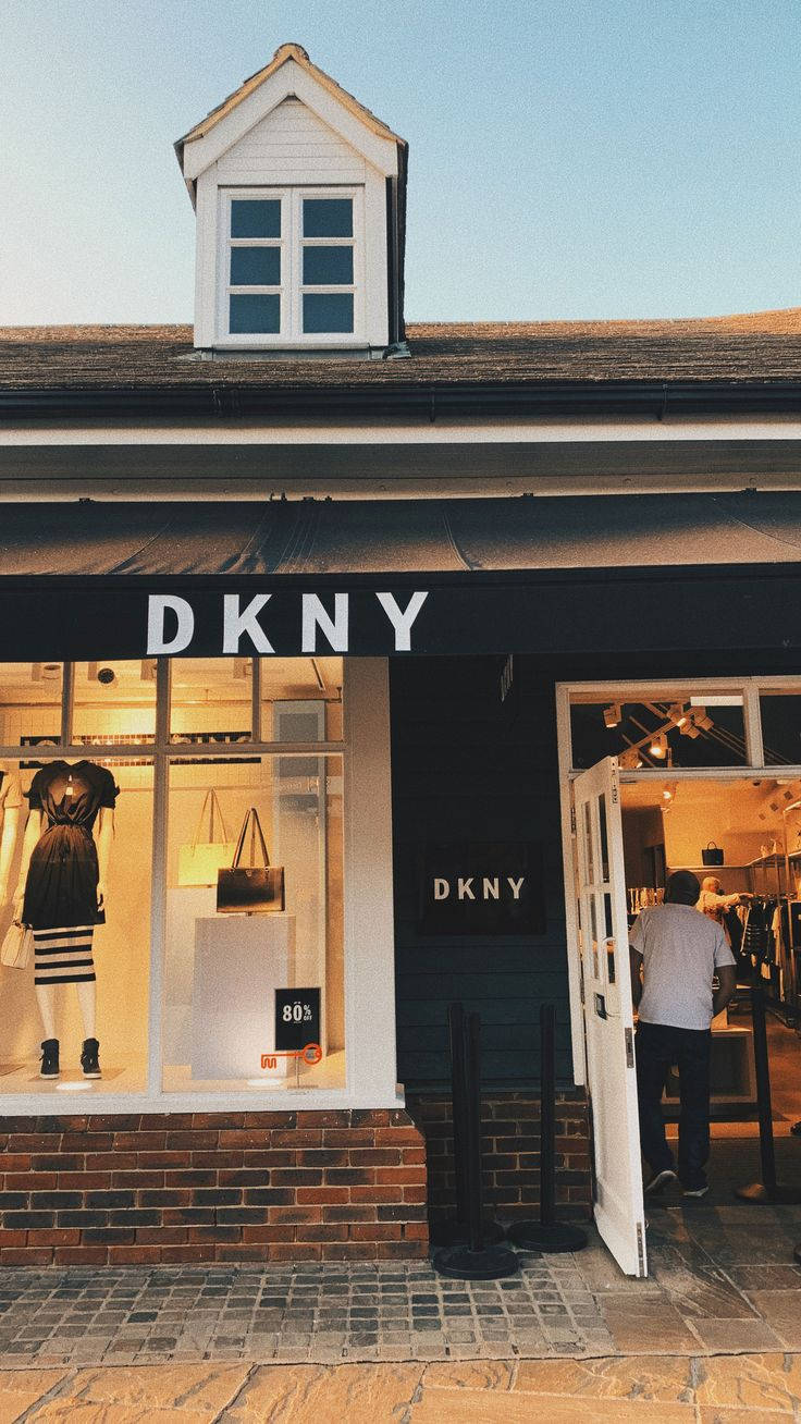 品牌 桌布 壁紙 — 黃昏時分的DKNY精品店，溫暖的室內燈光透過窗戶閃爍，一名男子正走進店內。