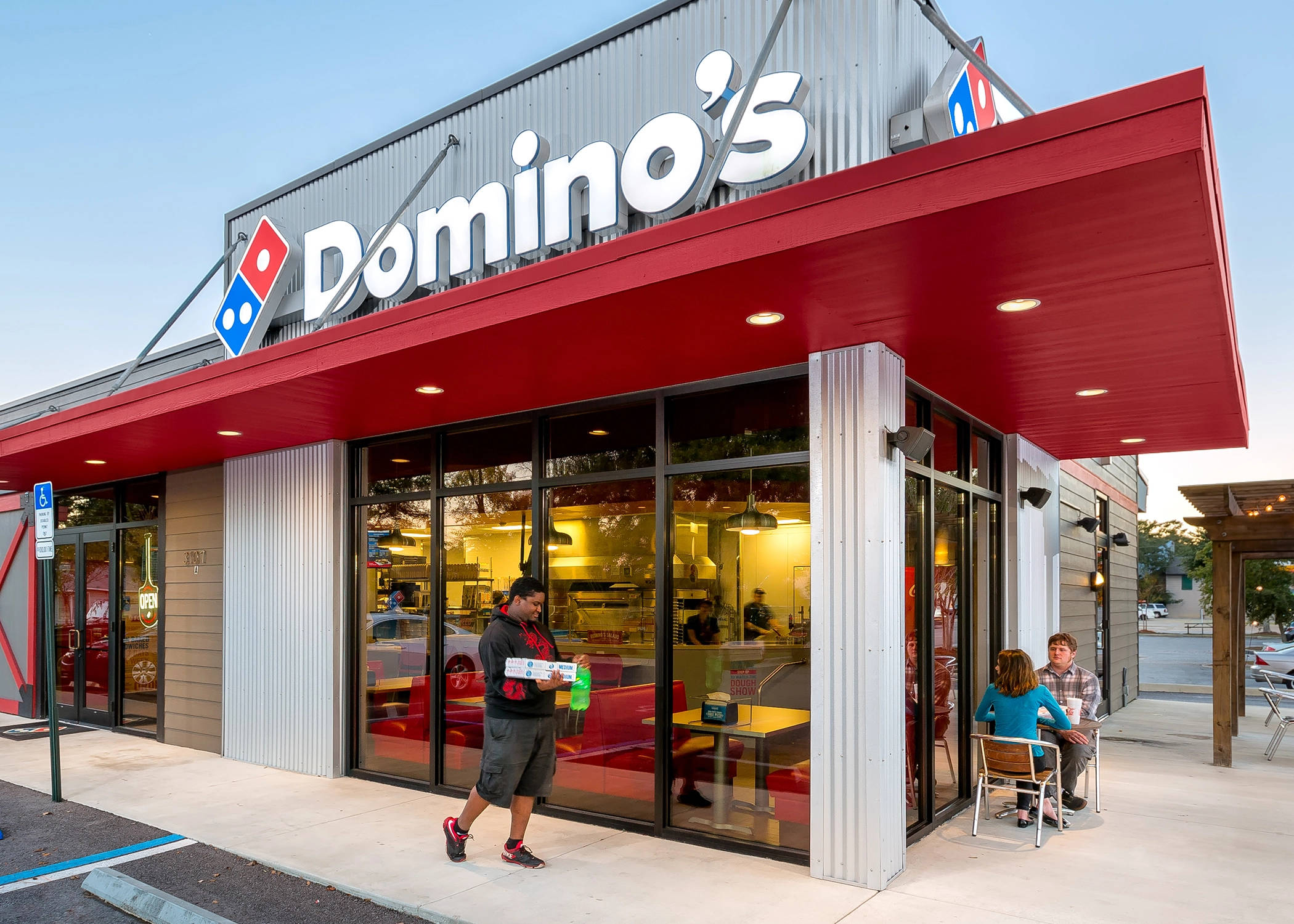 Building 桌布 壁紙 — 黃昏時分的Domino's披薩餐廳，有外送員經過，顧客坐在外面。