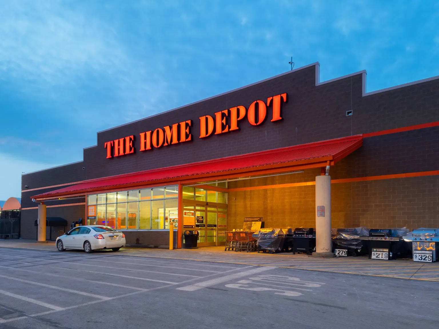 Home Depot 桌布 壁紙 — 黃昏時分的Home Depot商店，橙色發光招牌，藍天下停車場停著一輛白色汽車。