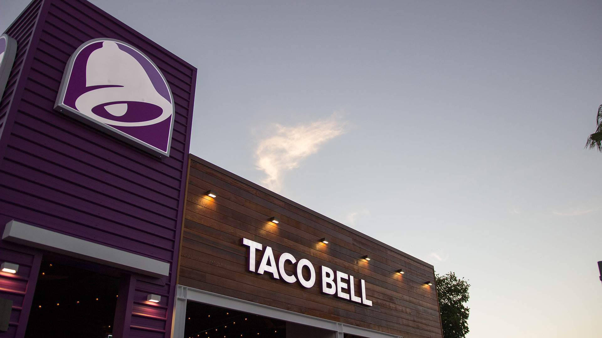 Taco Bell 桌布 壁紙 — 黃昏時分的Taco Bell餐廳，紫色牆板和發光招牌映襯著柔和天空。