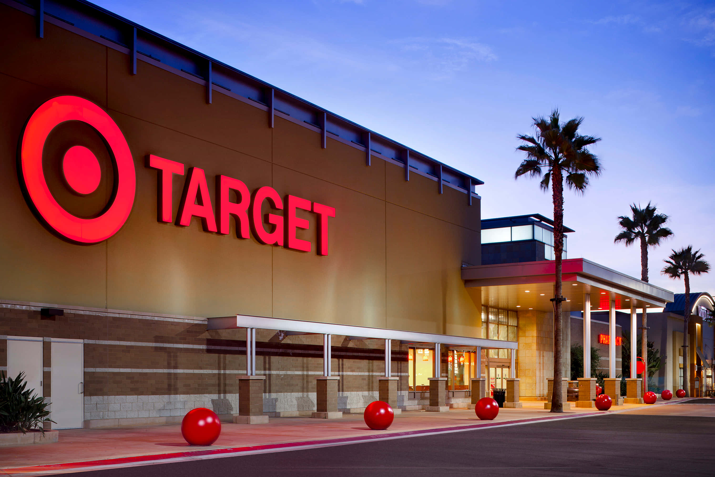 目標 桌布 壁紙 — 黃昏時分的Target商店建築，發光的紅色標誌、棕櫚樹和球形裝飾在暮色天空下。