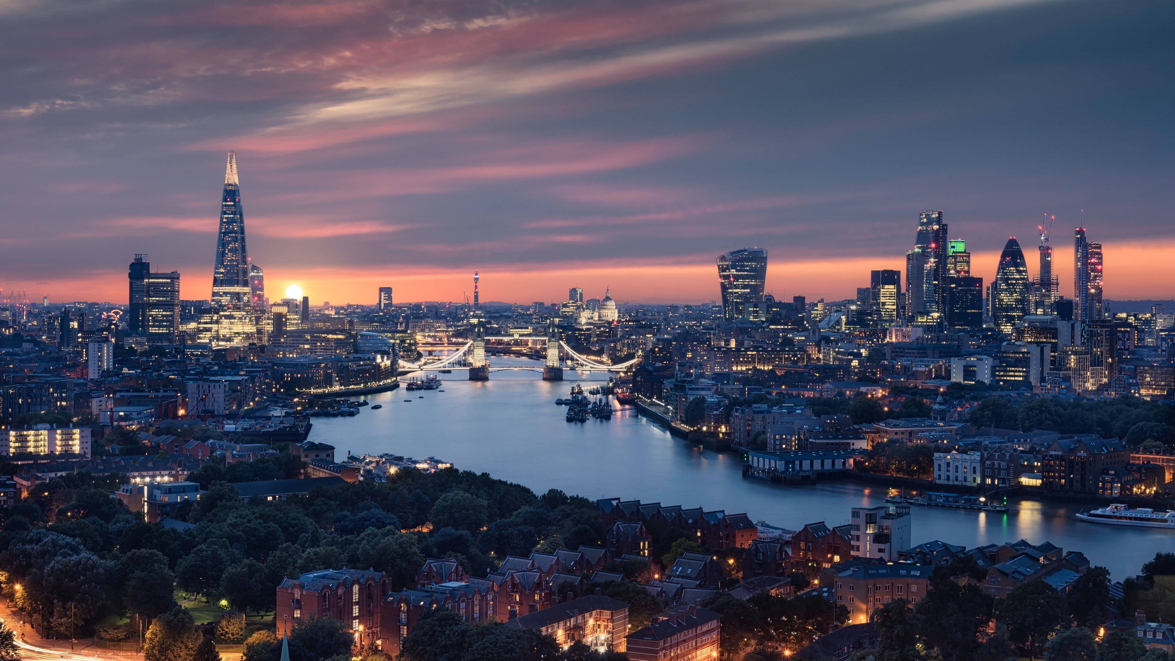 England 桌布 壁紙 — 黃昏時分的倫敦天際線，燈火通明的摩天大樓和泰晤士河反射出溫暖的橙色和紫色色調。