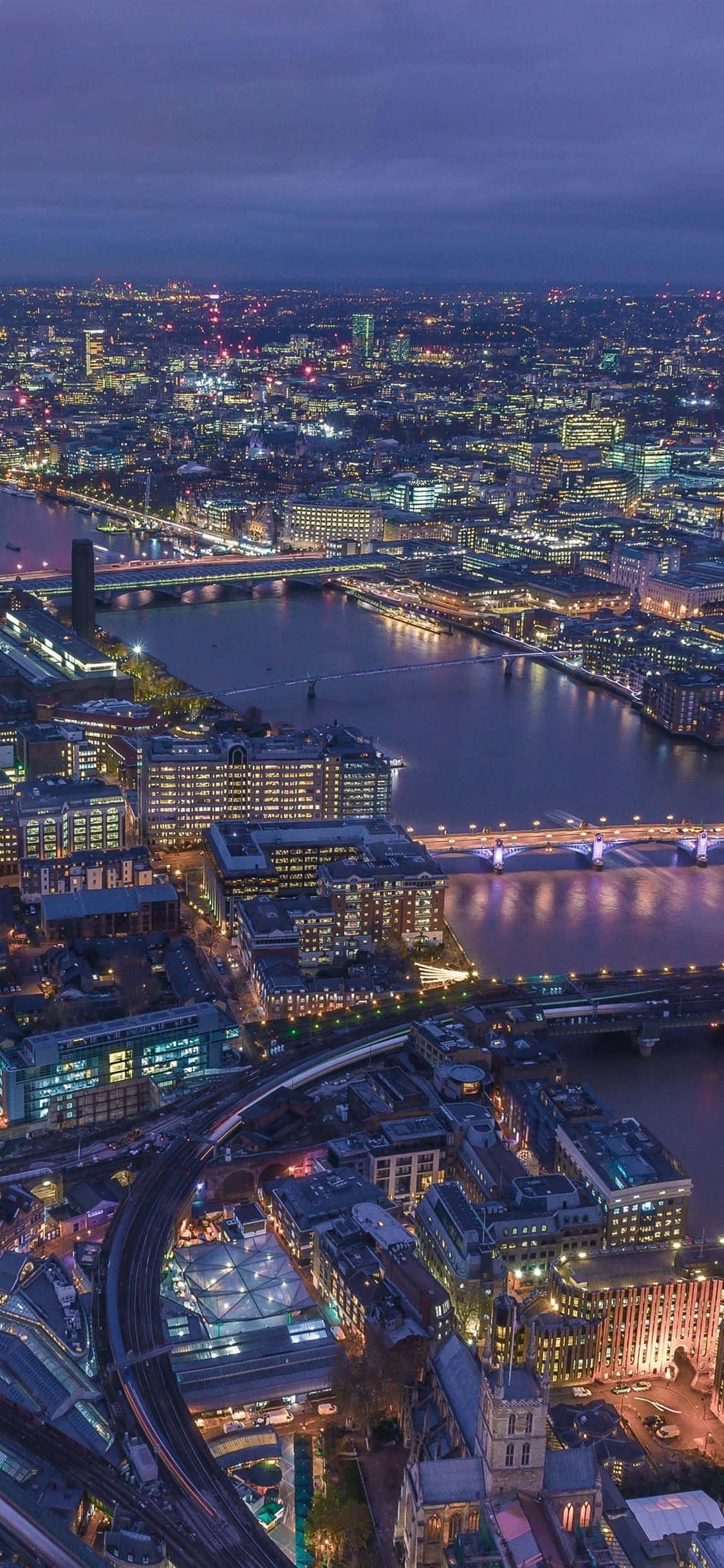 London iPhone 桌布 壁紙 — 黃昏時分的倫敦鳥瞰圖，城市燈光在泰晤士河和橋樑上閃爍倒映。