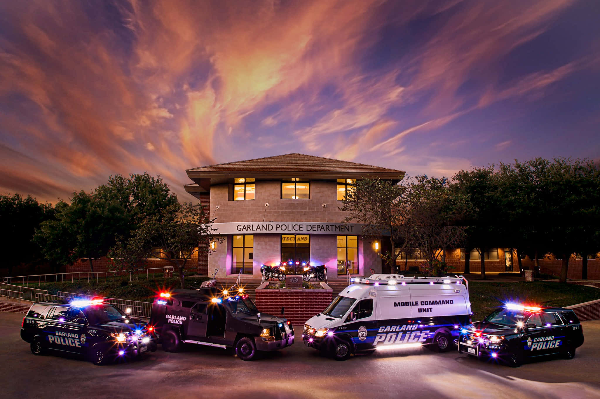 police lights 桌布 壁紙 — 黃昏時分的加蘭警察局大樓，四輛警車在火紅橙紫的天空下閃爍著警燈。