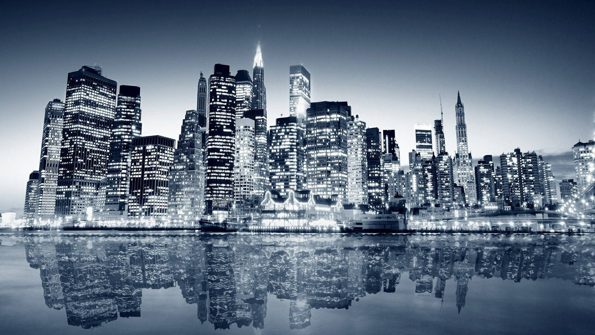 New York 桌布 壁紙 — 黃昏時分的單色城市天際線，摩天大樓在深藍色天空下閃耀，完美倒映在平靜的水面上。
