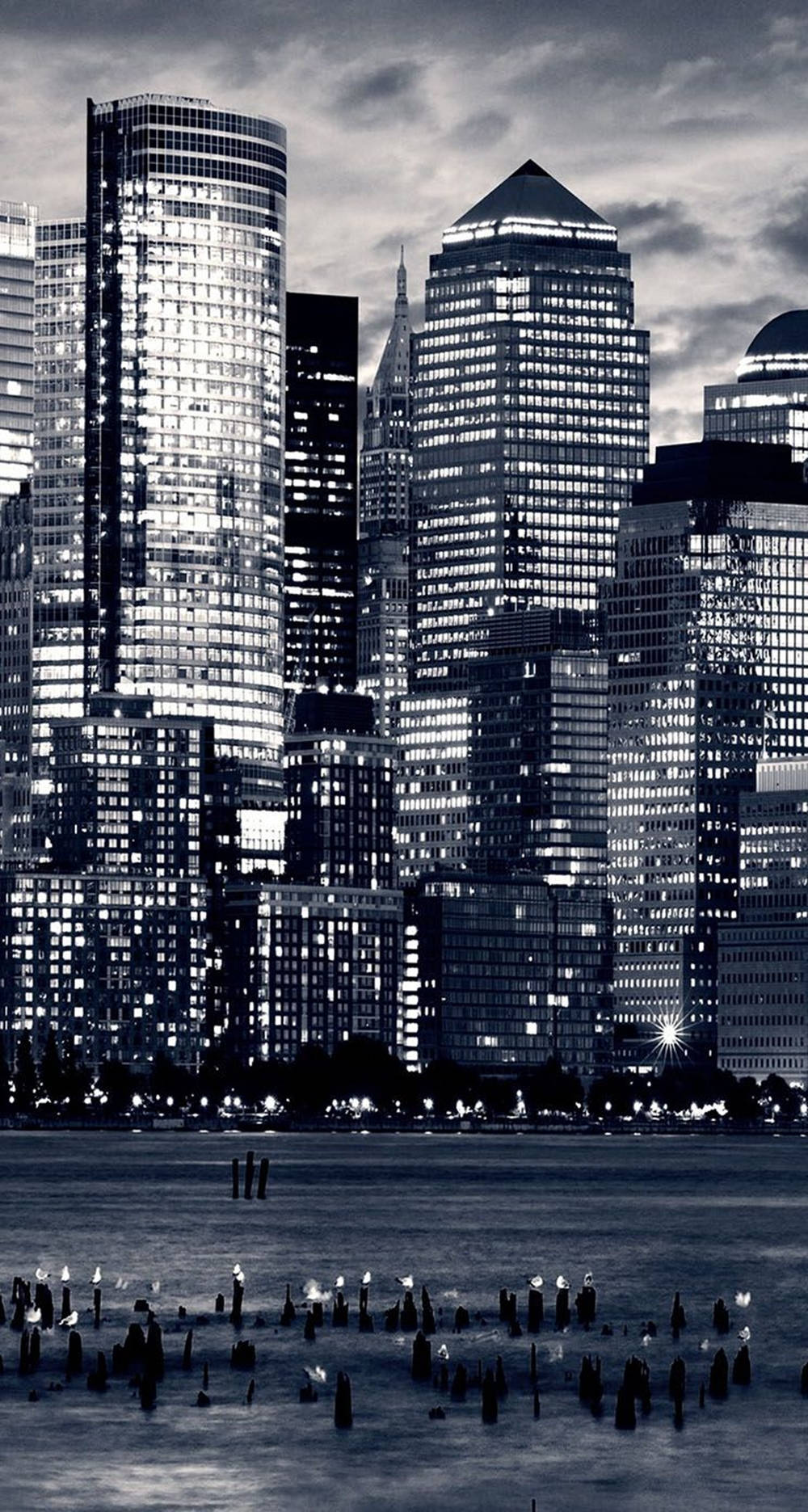 manhattan 桌布 壁紙 — 黃昏時分的單色城市天際線，發光的摩天大樓倒映在下方水中。