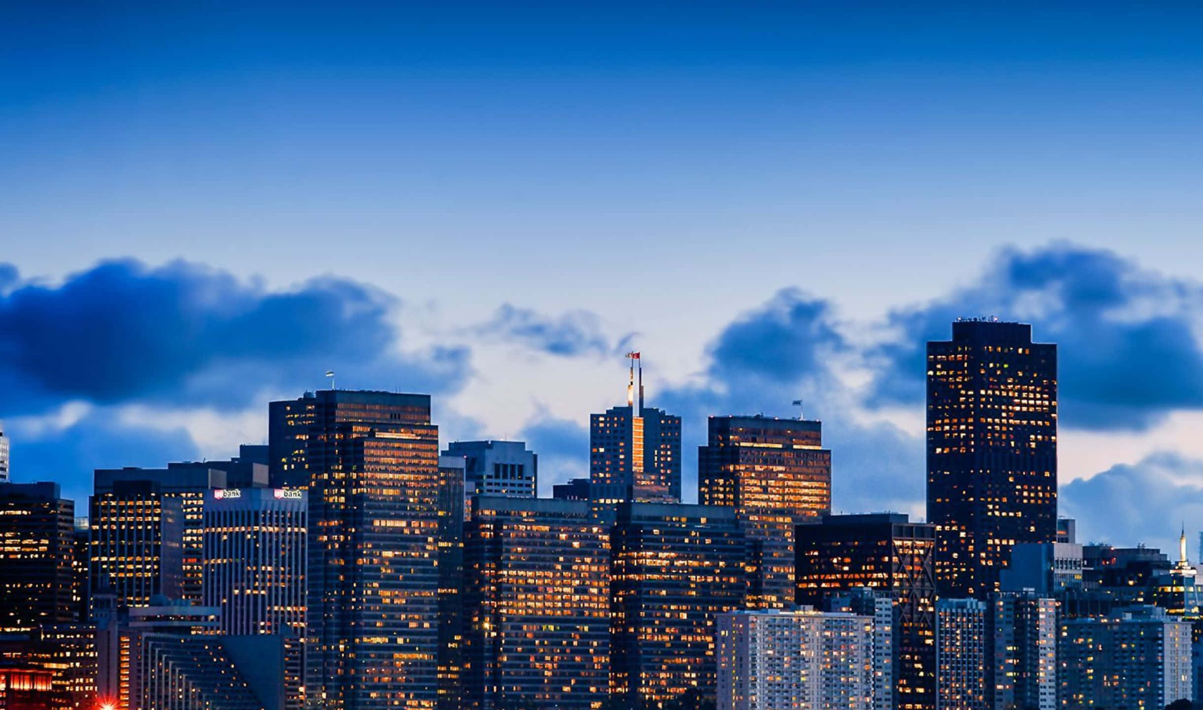 2440x1440 San Francisco 桌布 壁紙 — 黃昏時分的城市天際線，摩天大樓在深藍色天空和散落的雲朵映襯下閃爍燈光。