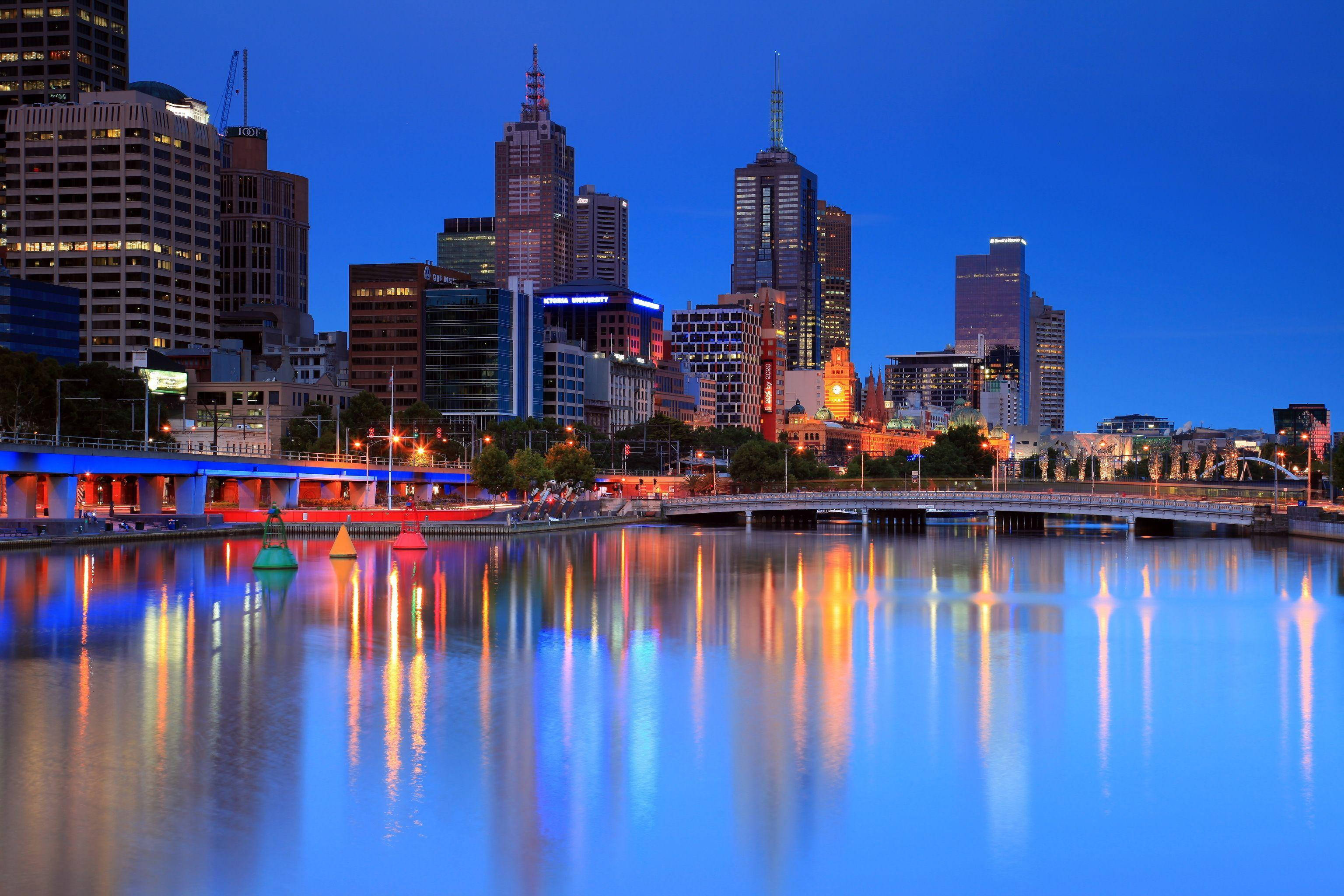 Melbourne 桌布 壁紙 — 黃昏時分的城市天際線，摩天大樓在深藍色天空下倒映在平靜的河水上。
